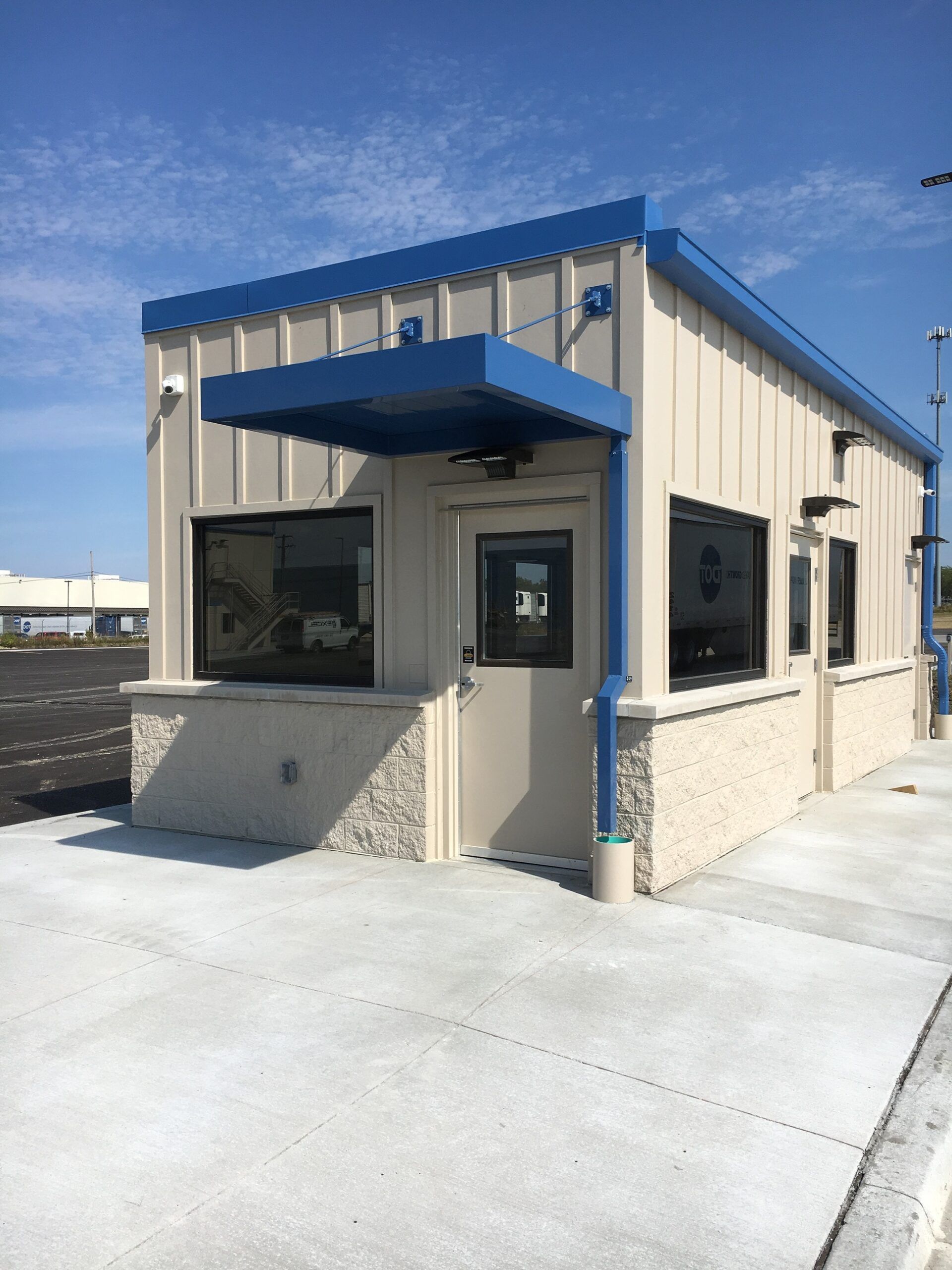 Small beige building with blue trim and awning on a concrete lot under a clear sky
