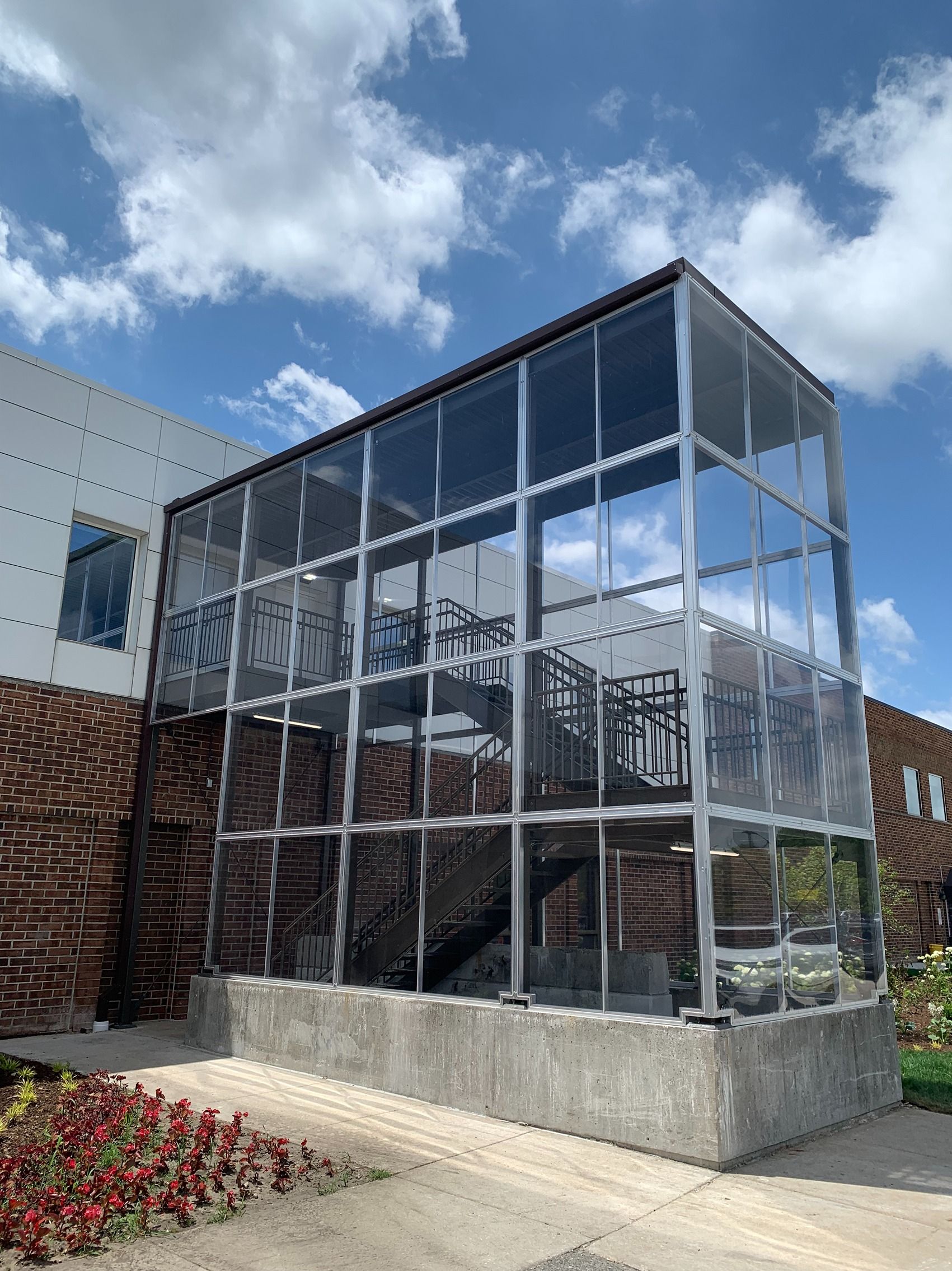 Modern glass atrium on a concrete base beside a brick building under a blue sky