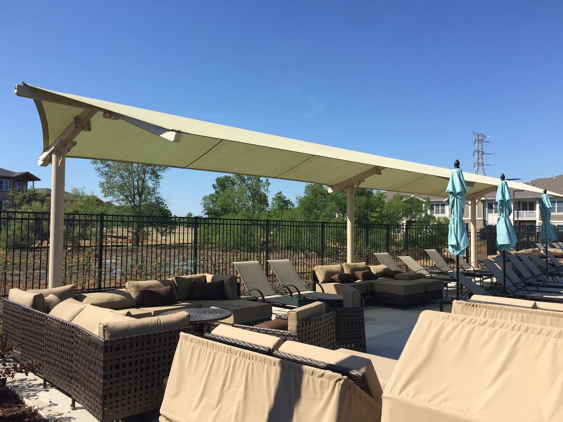 Outdoor patio seating with beige couches, umbrellas, and a green canopy on a sunny day