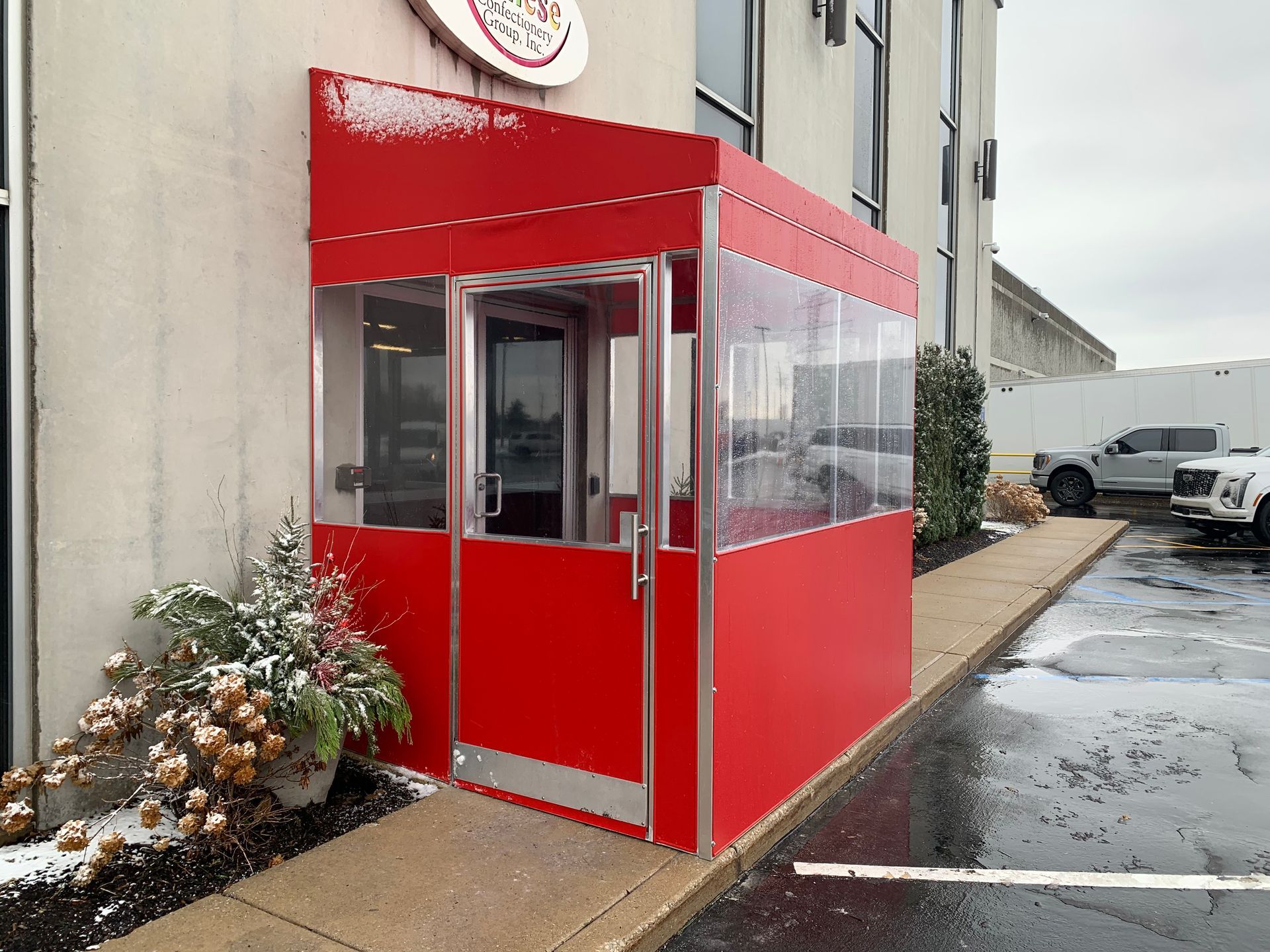 Red storefront entrance with glass canopy beside a wet parking lot.