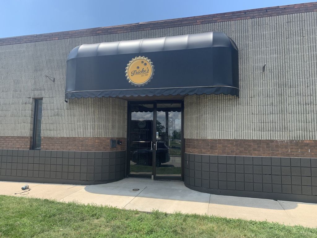 Building entrance with dark blue awning and glass door in a tan brick exterior.