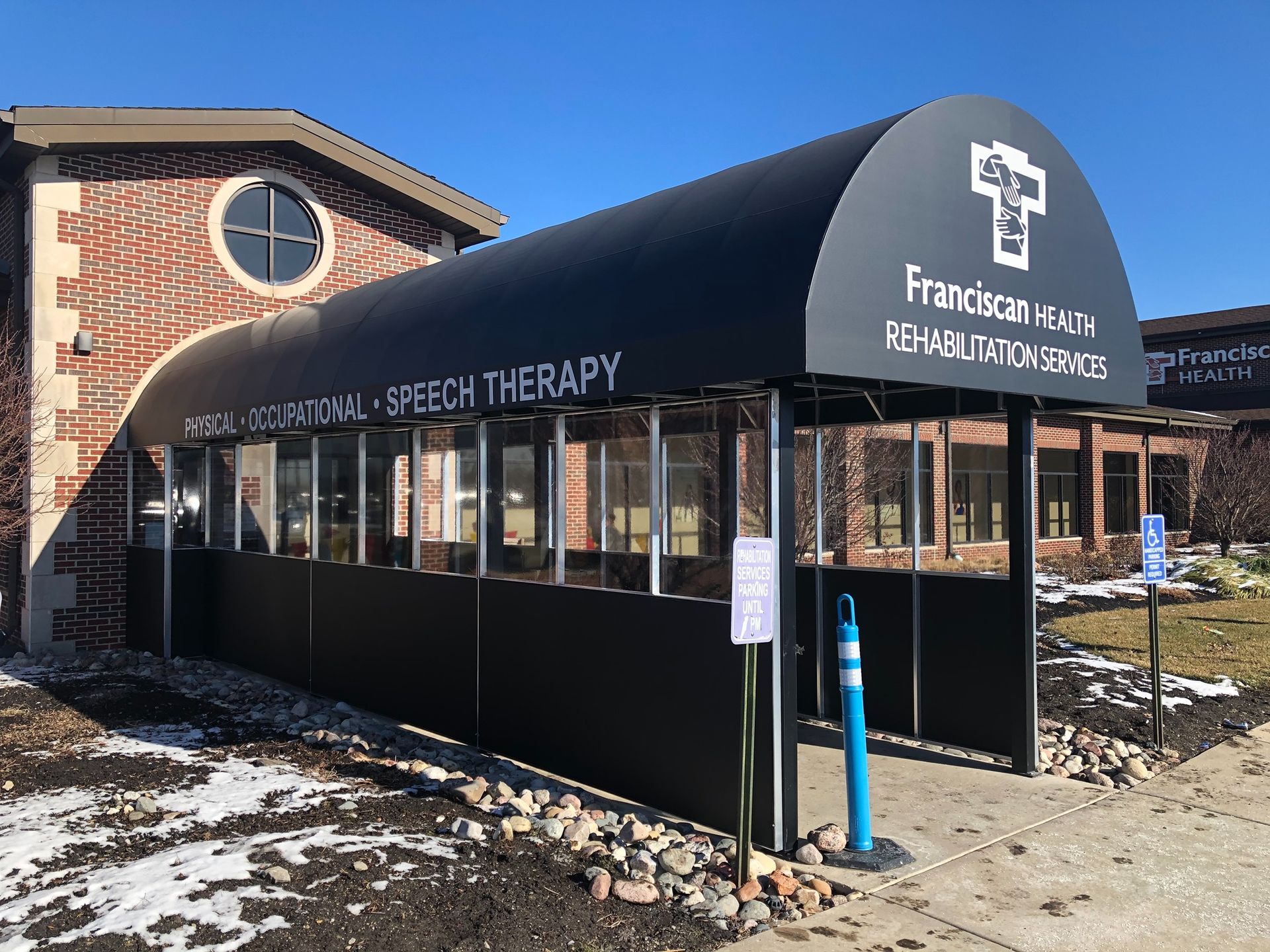 Franciscan Rehabilitation Center entrance with black awning, brick building, and snow on the ground