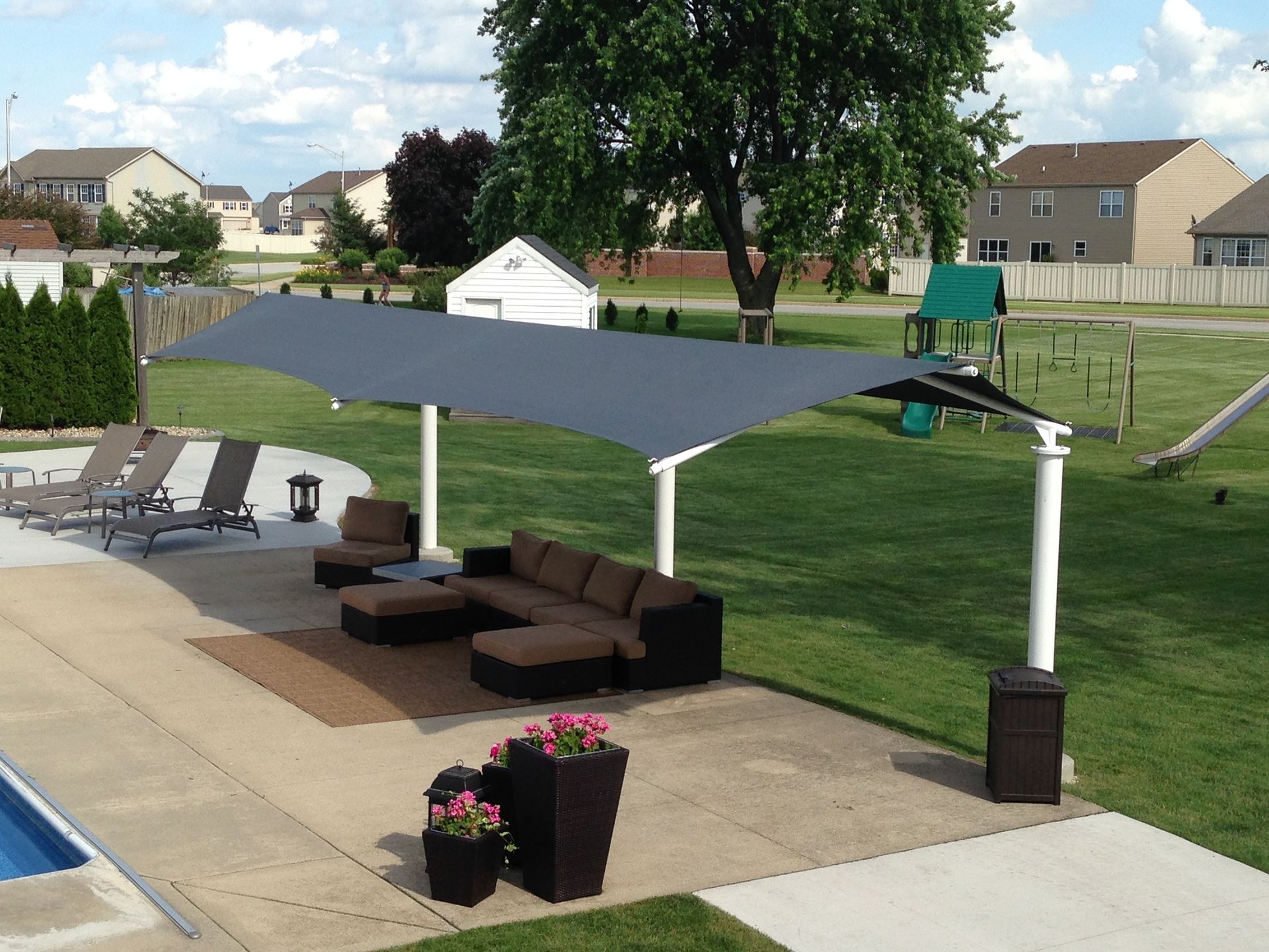Backyard patio with gray canopy, lounge chairs, cushioned seating, and a pool beside a grassy lawn.