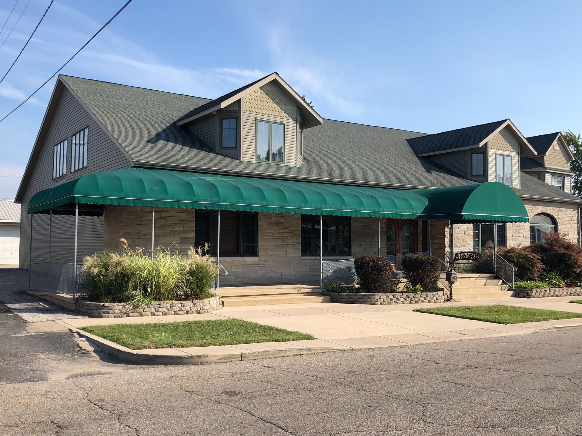 Two-story stone building with green awnings and a sidewalk in front