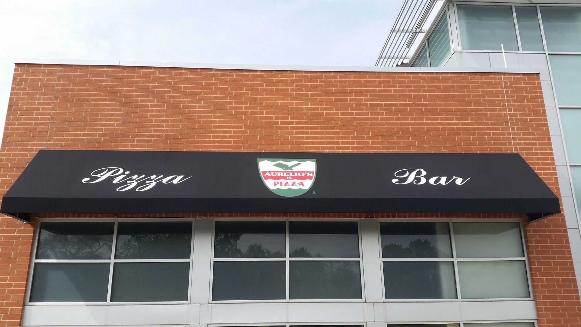 Black awning on brick building reads “Pizza Bar” above storefront windows.