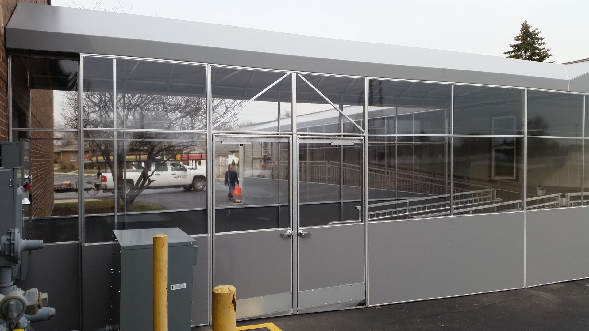 Glass bus shelter with metal frame and doors beside a sidewalk, with a person inside.