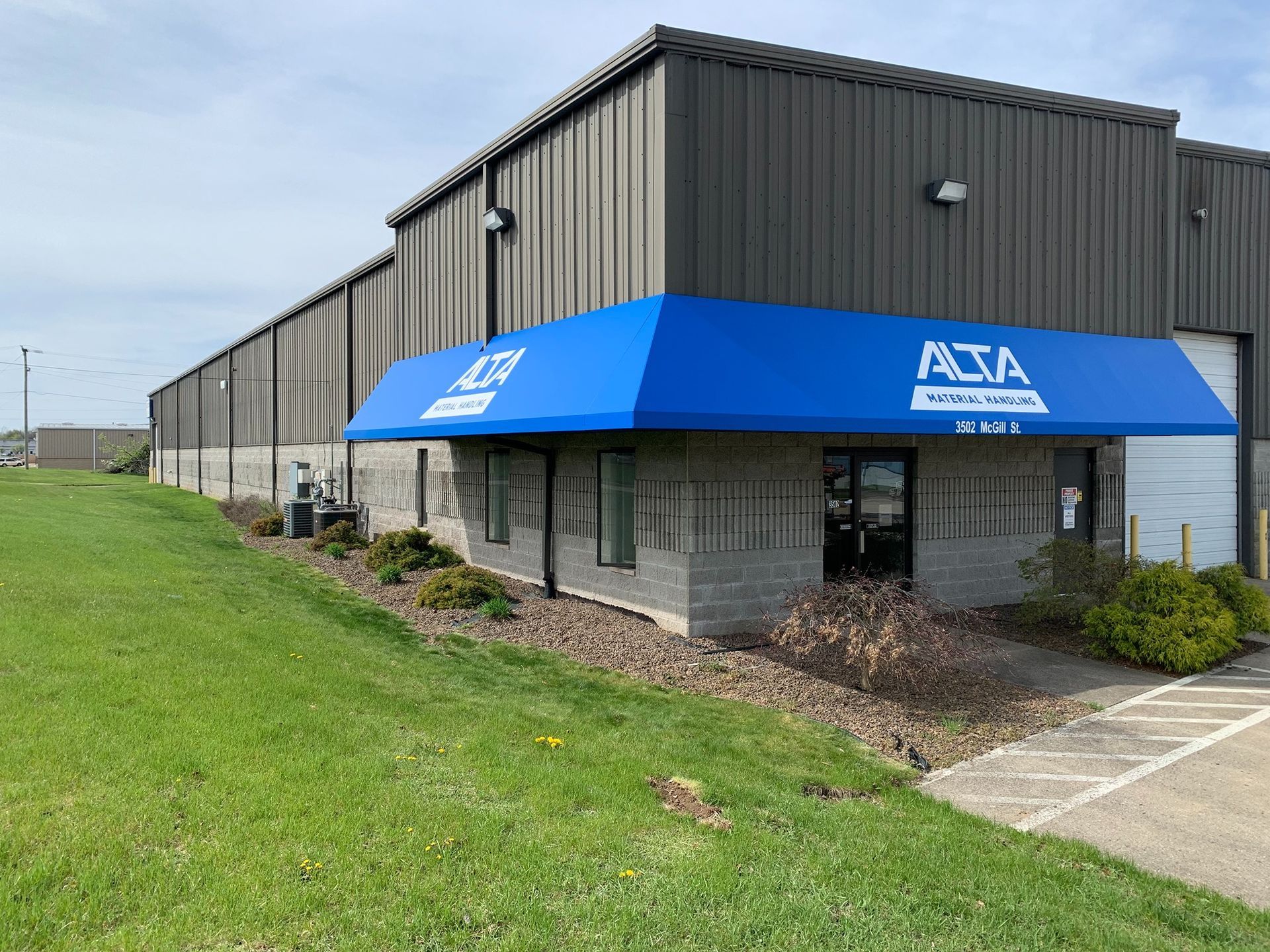 Industrial building with a blue awning and ATA branding beside a grassy lot