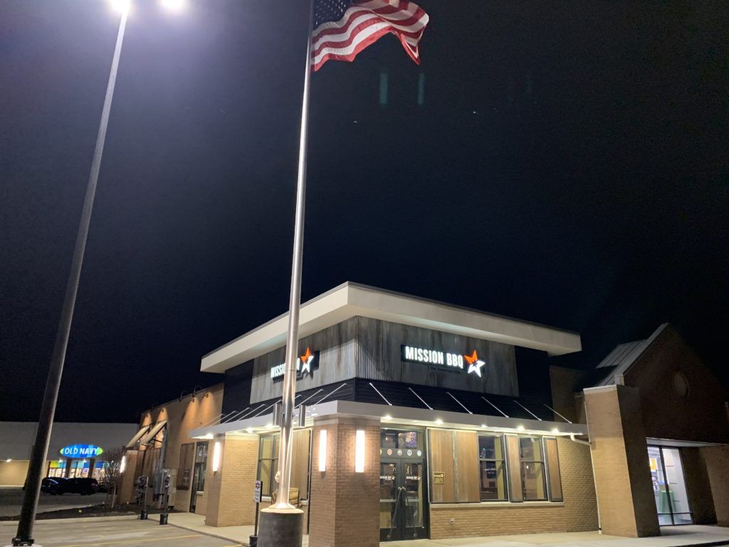Fast-food restaurant at night with lit sign, flagpoles, and illuminated exterior.