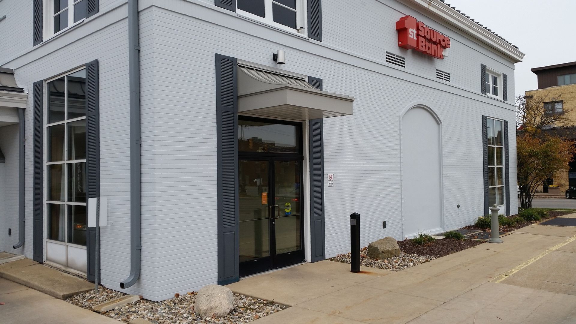 Corner view of a white storefront with a glass entrance and red sign beside a sidewalk