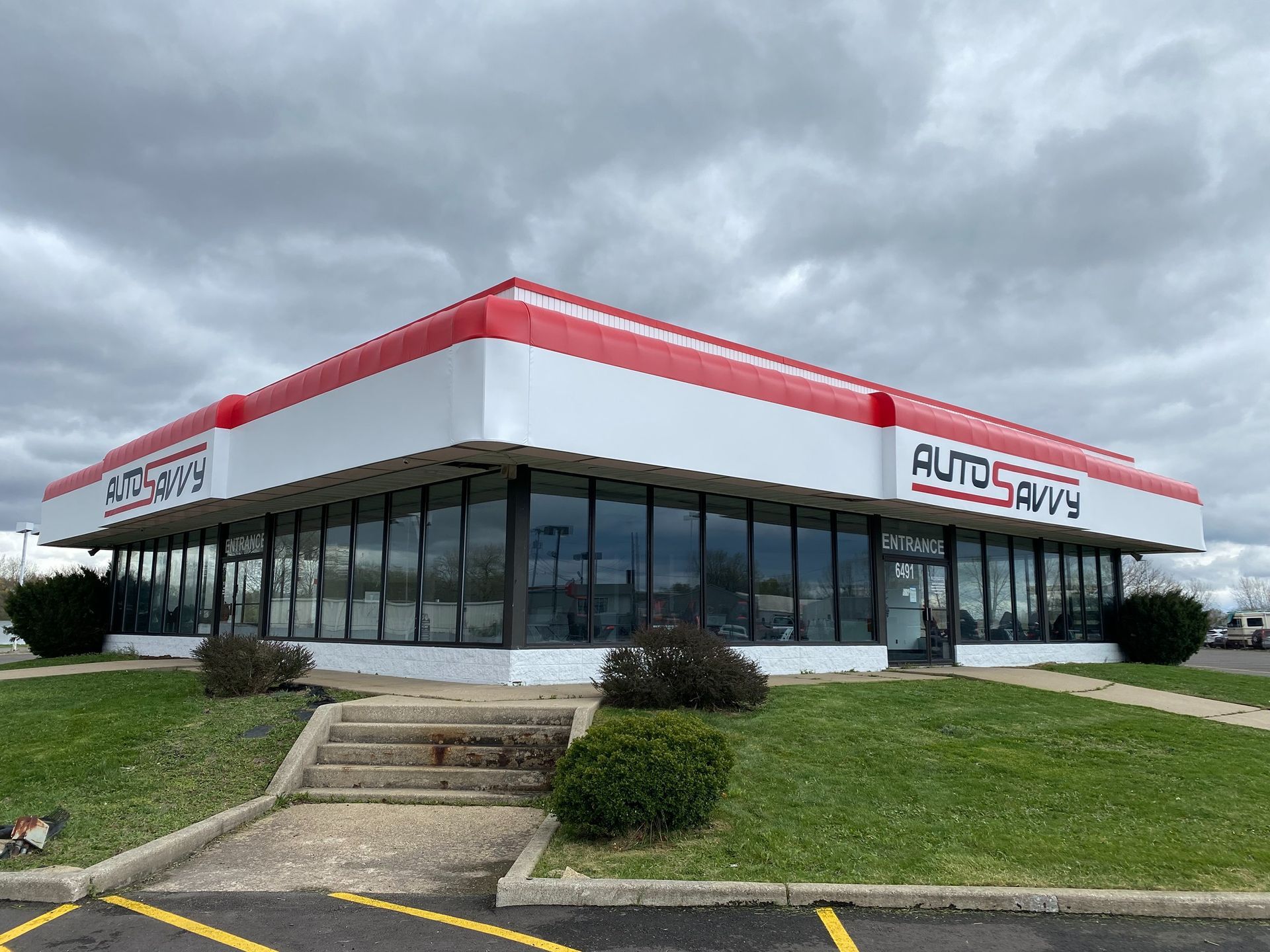 Auto Savvy car dealership with glass windows, red trim, and cloudy sky
