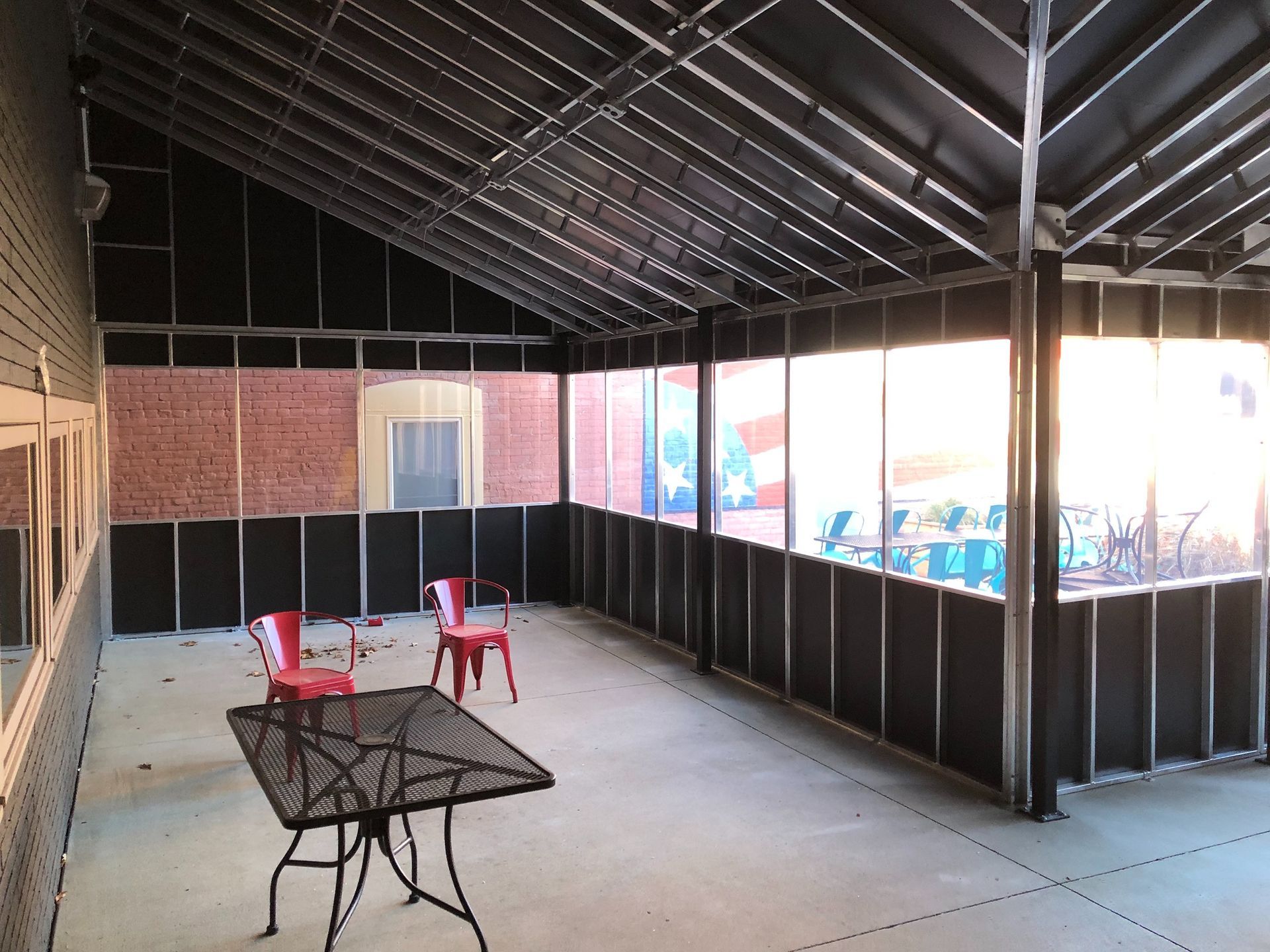 Covered patio with black railing, small table, and red chairs under a metal roof