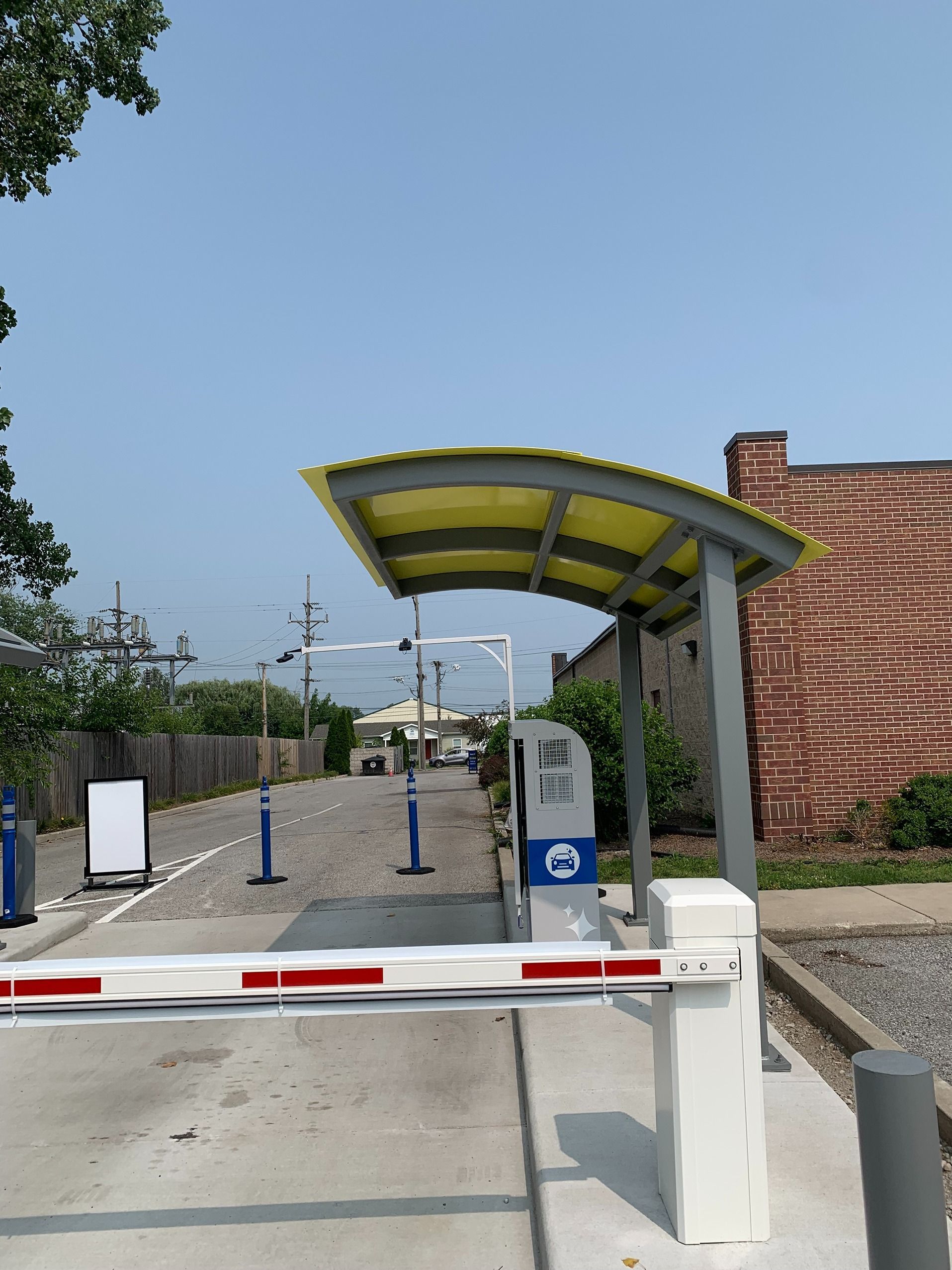 Entrance gate with barrier arm and yellow canopy at a fenced facility under a clear blue sky