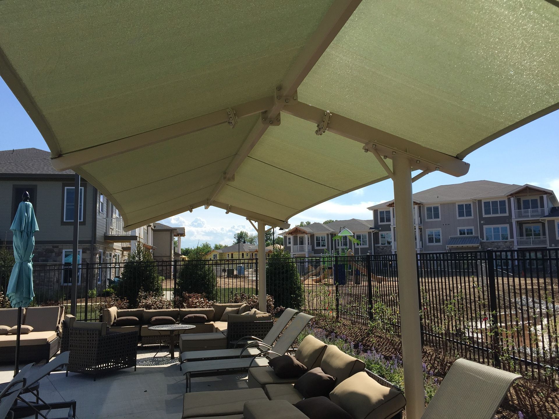 Shaded outdoor patio with lounge chairs, umbrella tables, and apartment buildings in the background