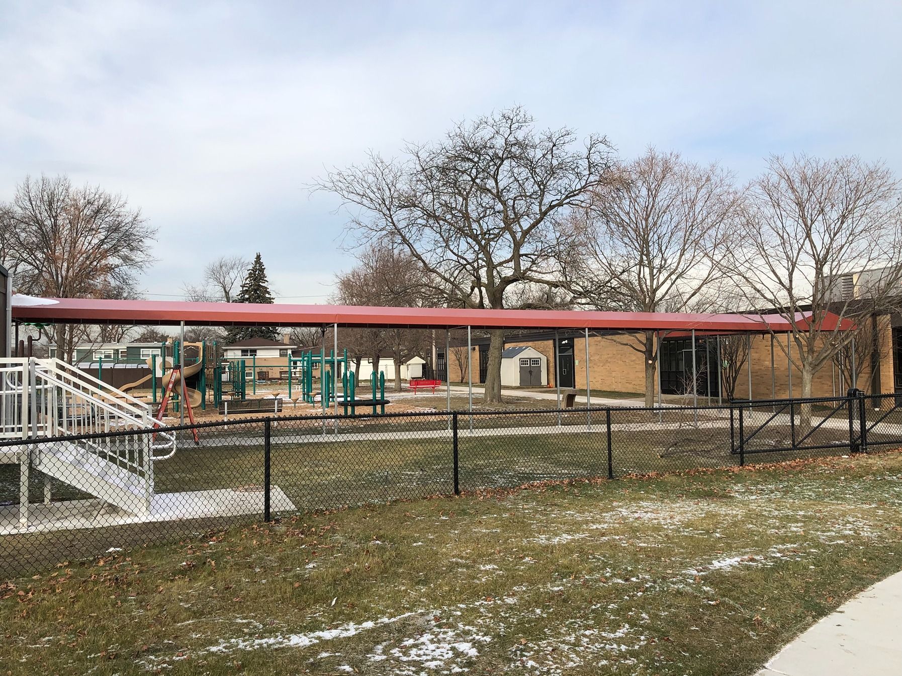 School playground behind a black fence, with red-roofed play structures and bare trees on a winter day