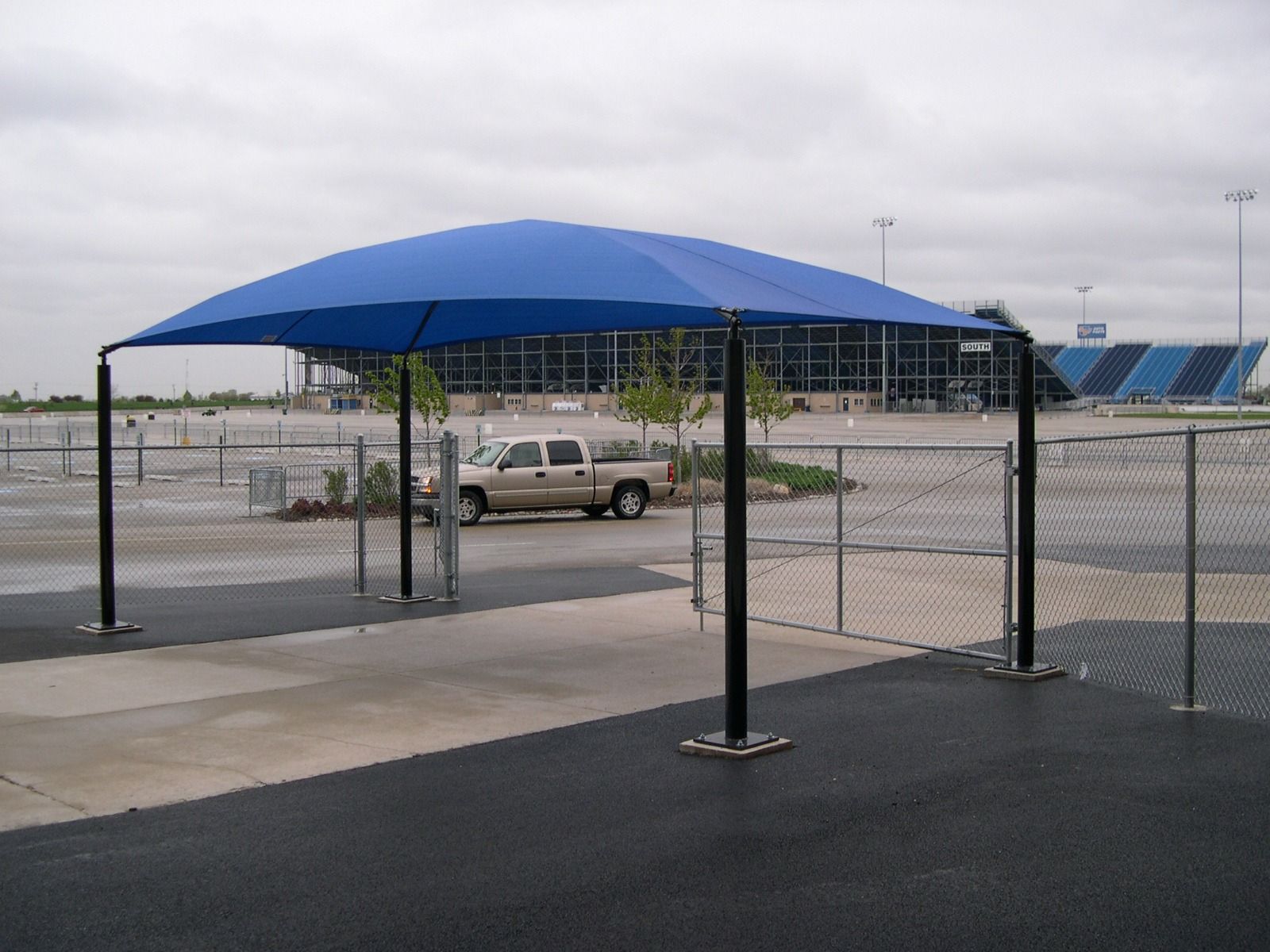 Blue shade canopy over a parking lot beside a chain-link fence and parked van.