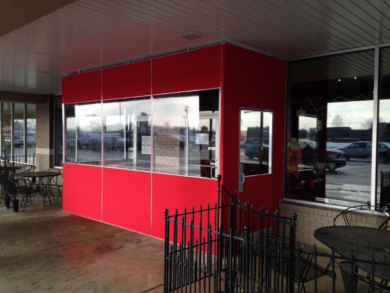 Red outdoor patio booth with large windows and black metal tables under a covered walkway