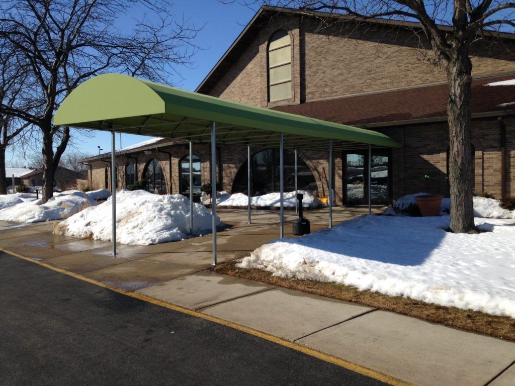 Covered walkway beside a brick building with snow on the ground and bare trees nearby