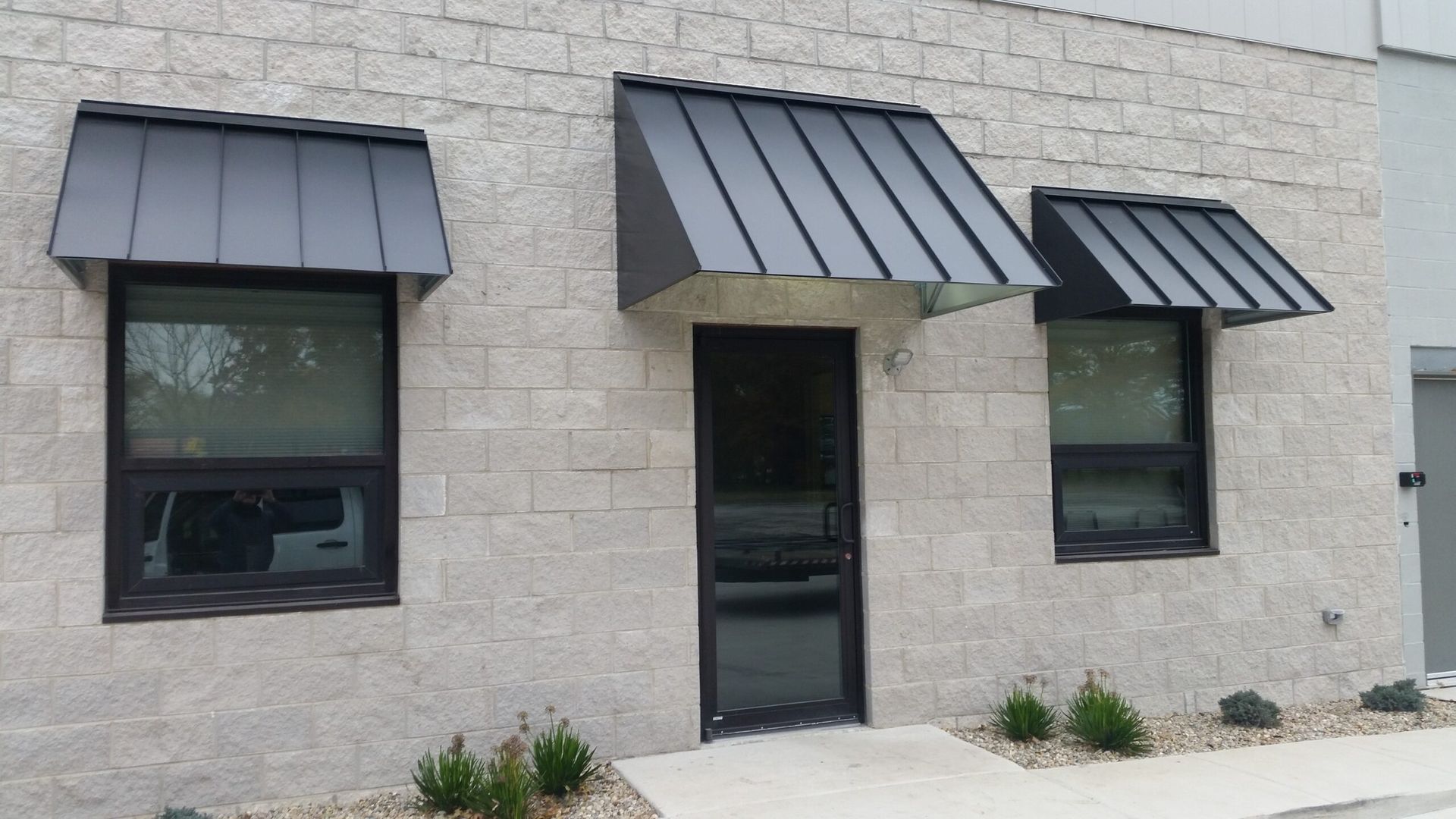 Exterior of a light stone building with black awnings over two windows and a central door