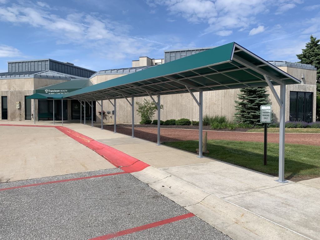 Covered walkway with green canopy leading to a building entrance beside a red curb and sidewalk
