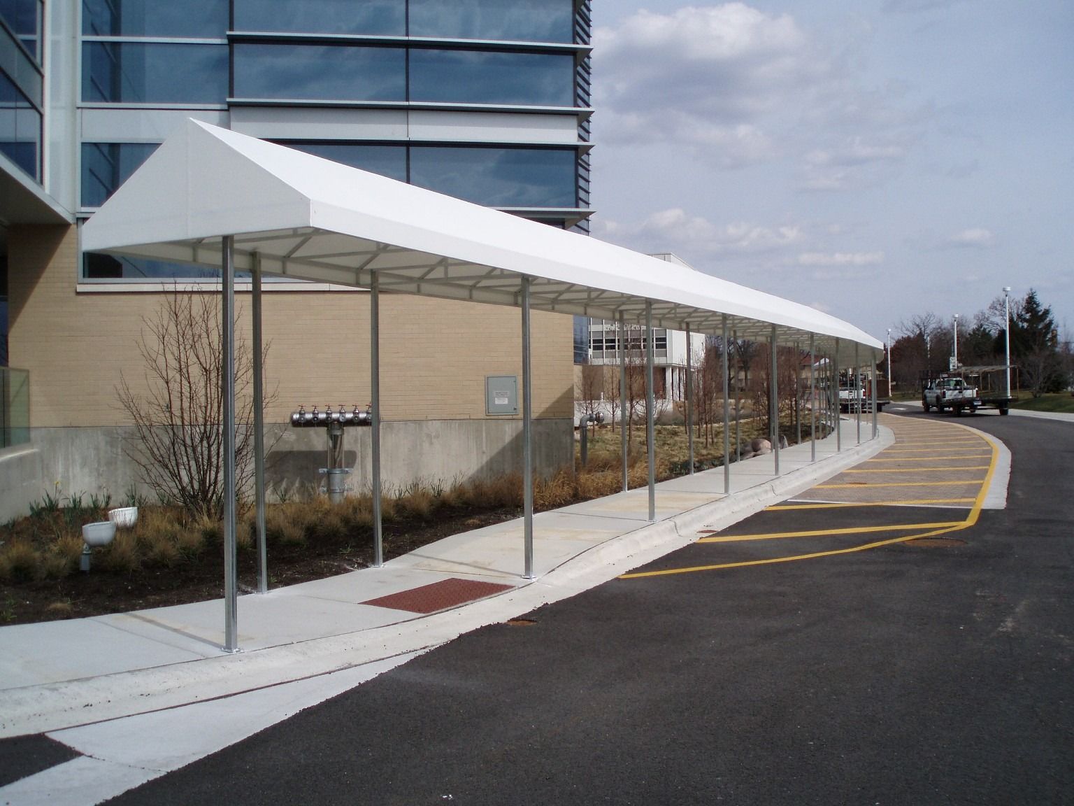 Covered sidewalk beside a building with a long white canopy along a curved road
