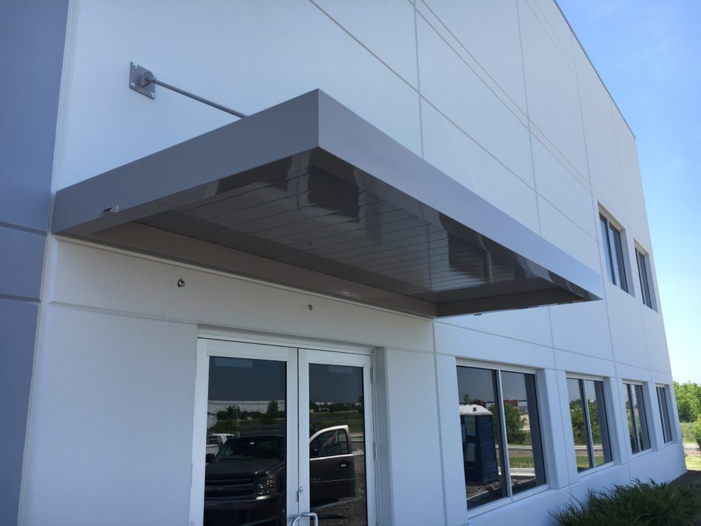 Modern building entrance with glass doors, white facade, and a large metal awning