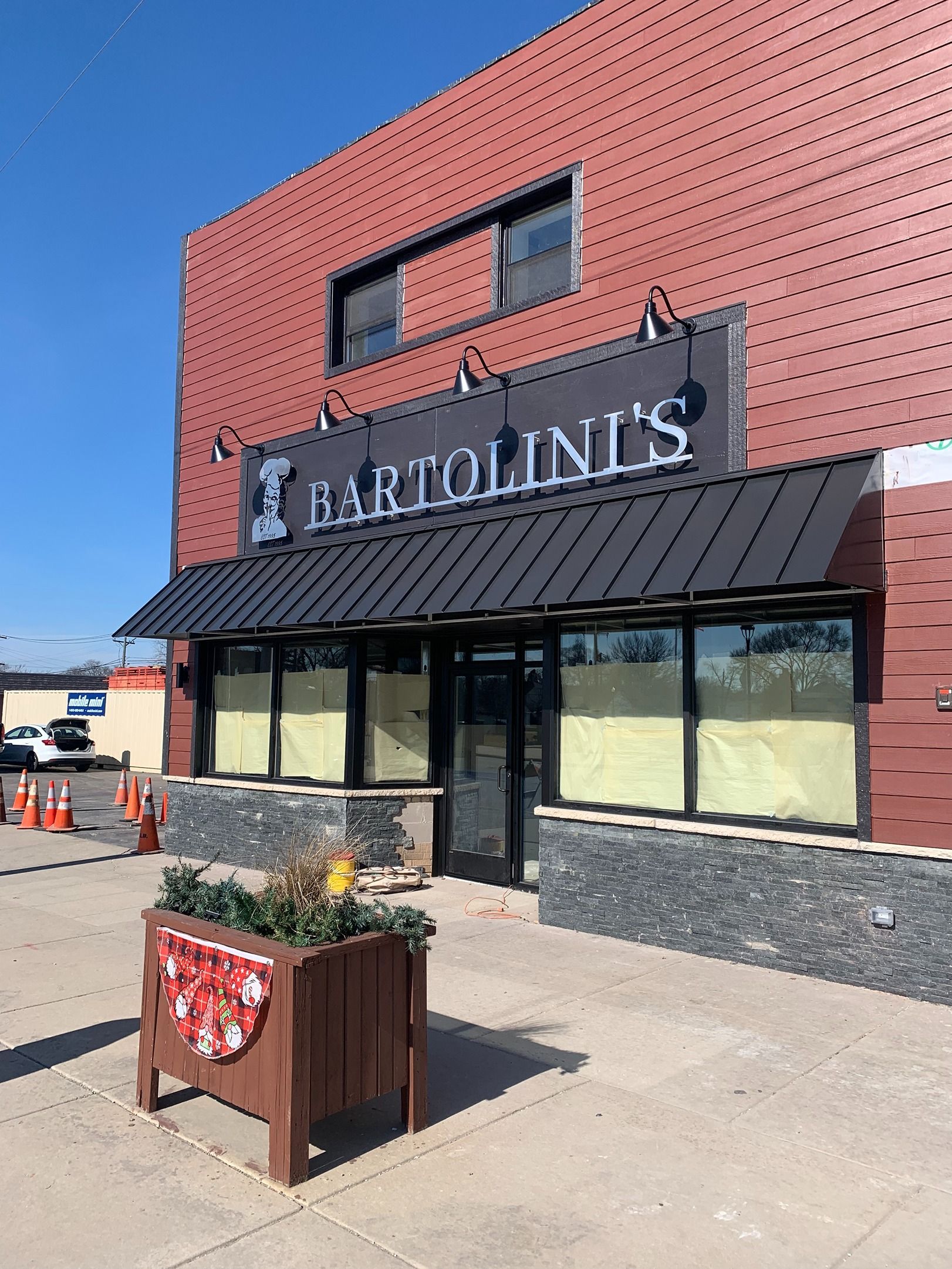 Front of Harlow’s restaurant with red brick facade, black awning, and planter by the sidewalk