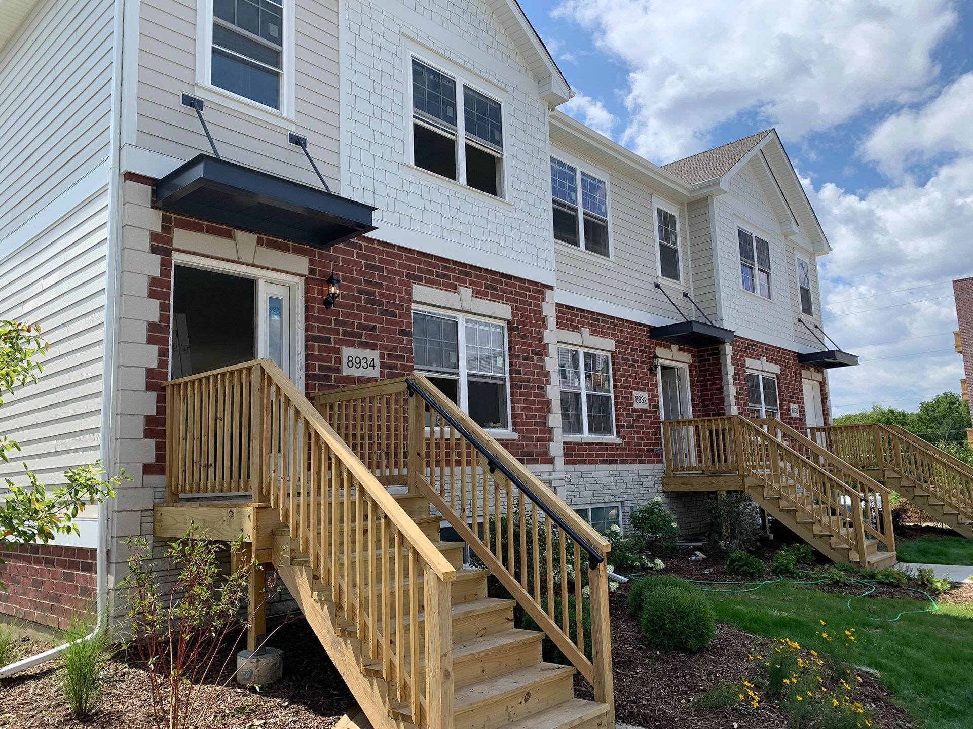 Row of townhouses with wooden front steps and small landscaped yards under a partly cloudy sky