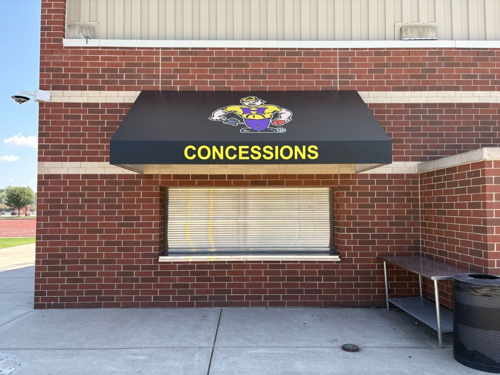 Closed concession stand with black awning and yellow sign against a red brick wall