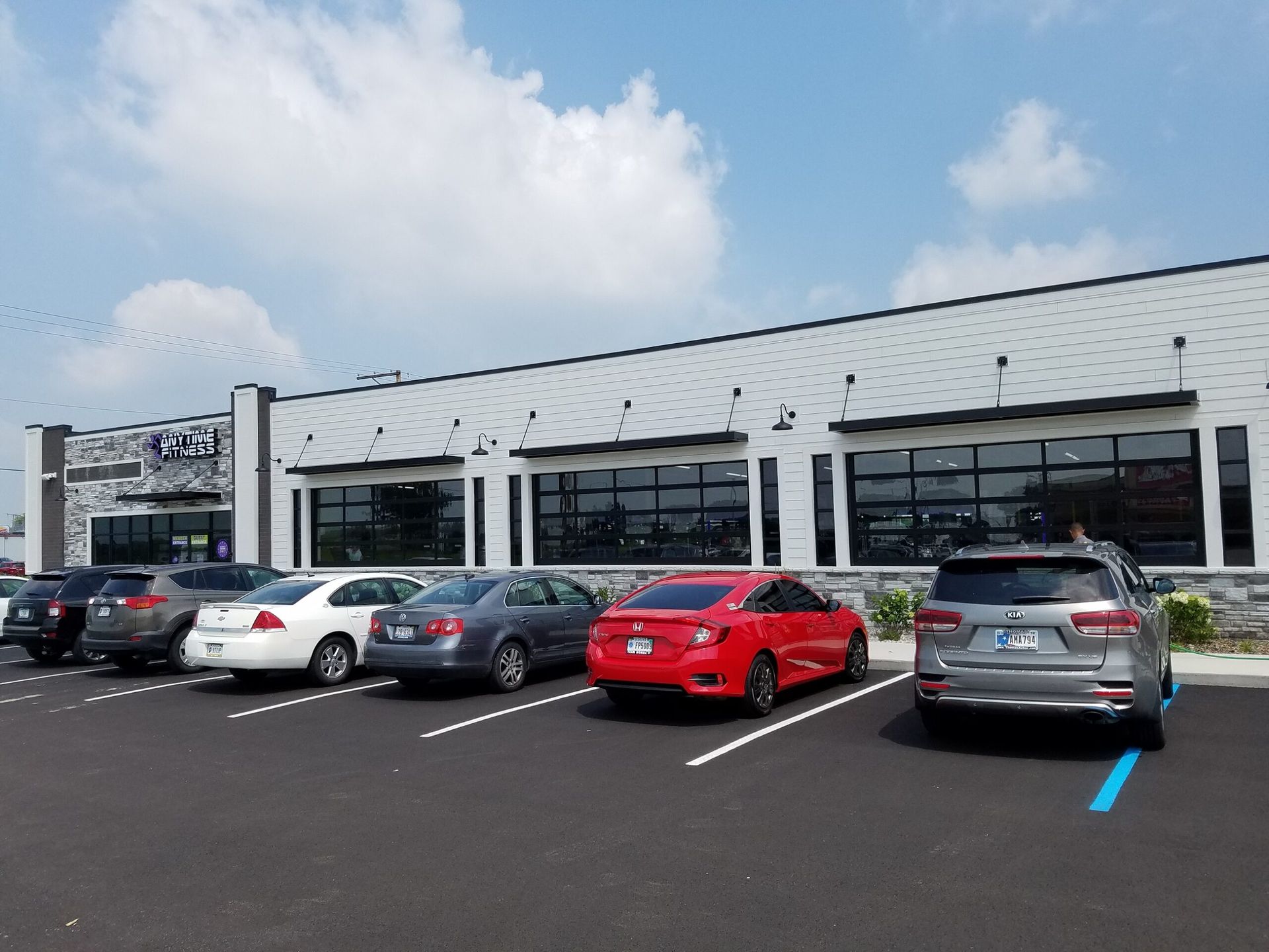 Parking lot outside a low commercial building with several parked cars under a blue sky.