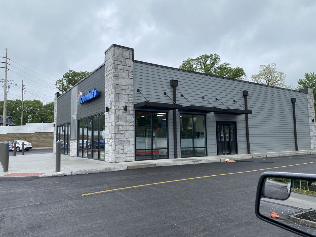 Small gray-and-black fast-food restaurant with glass windows and a drive-thru lane under a cloudy sky