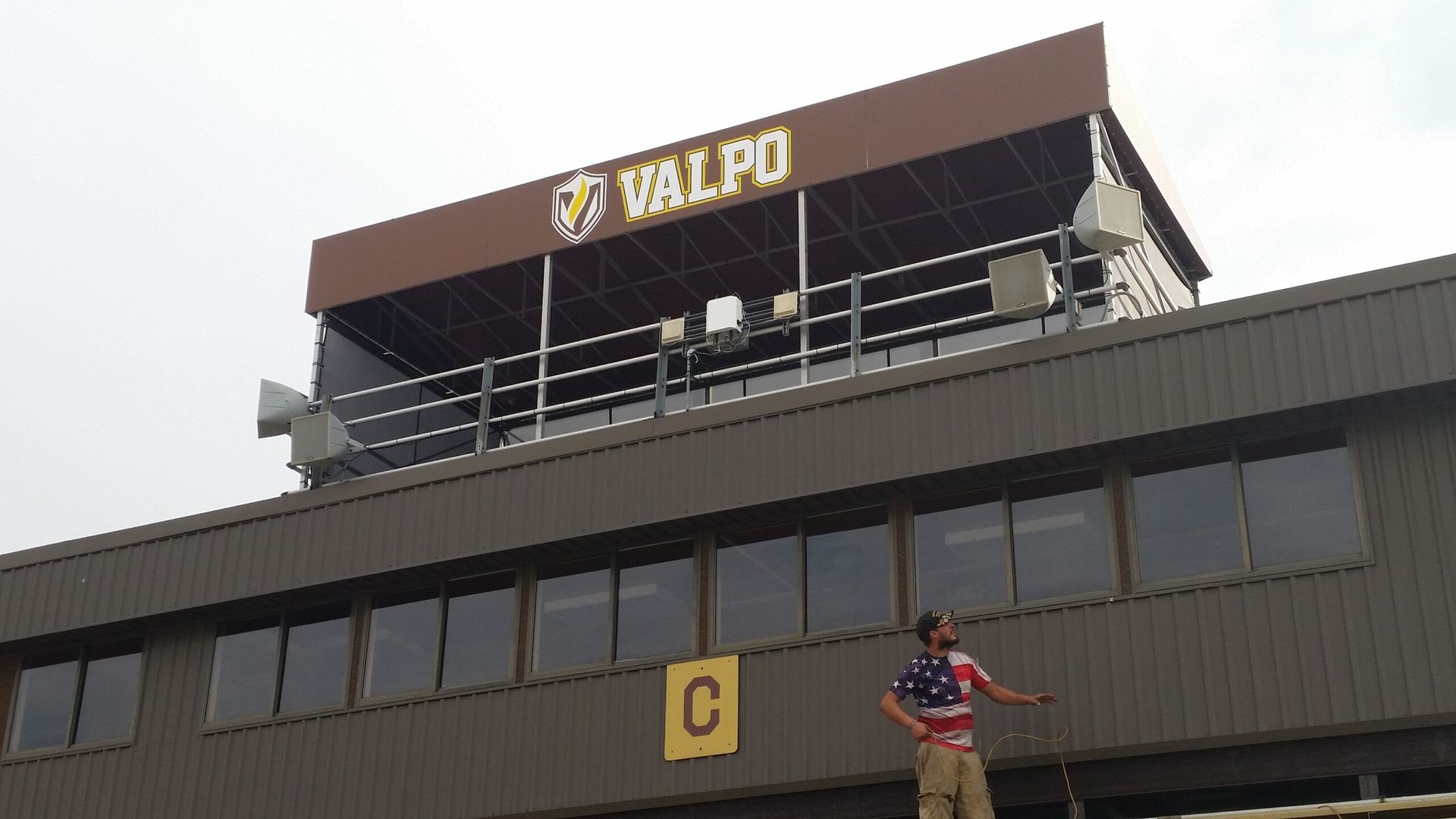 A stadium scoreboard and upper deck with a person standing below, wearing a red shirt and beige pants.