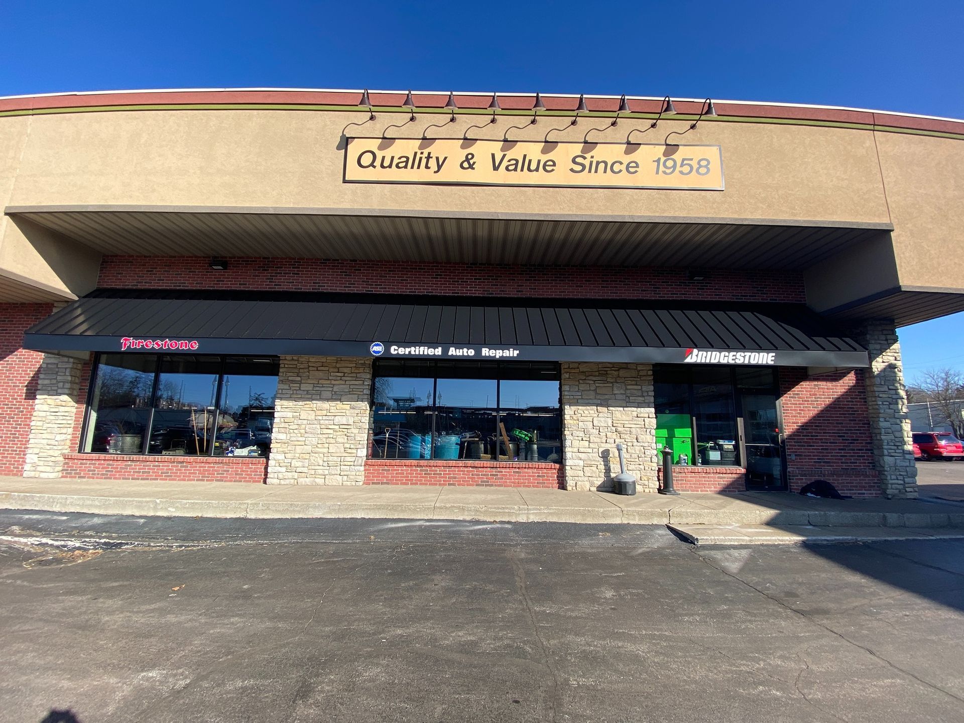 Strip mall storefront with tan facade, brick columns, and “Quality & Value Since 1958” sign above windows.