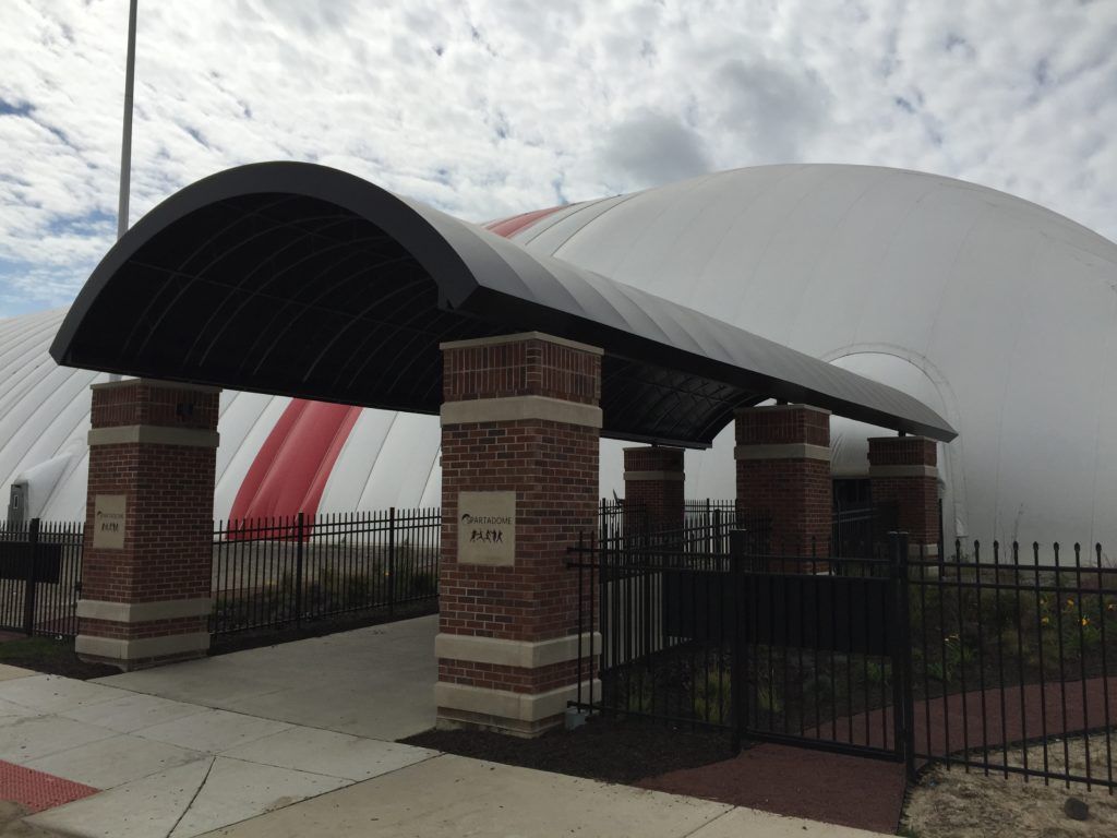 Covered entrance with brick pillars and black gates in front of a large white dome structure