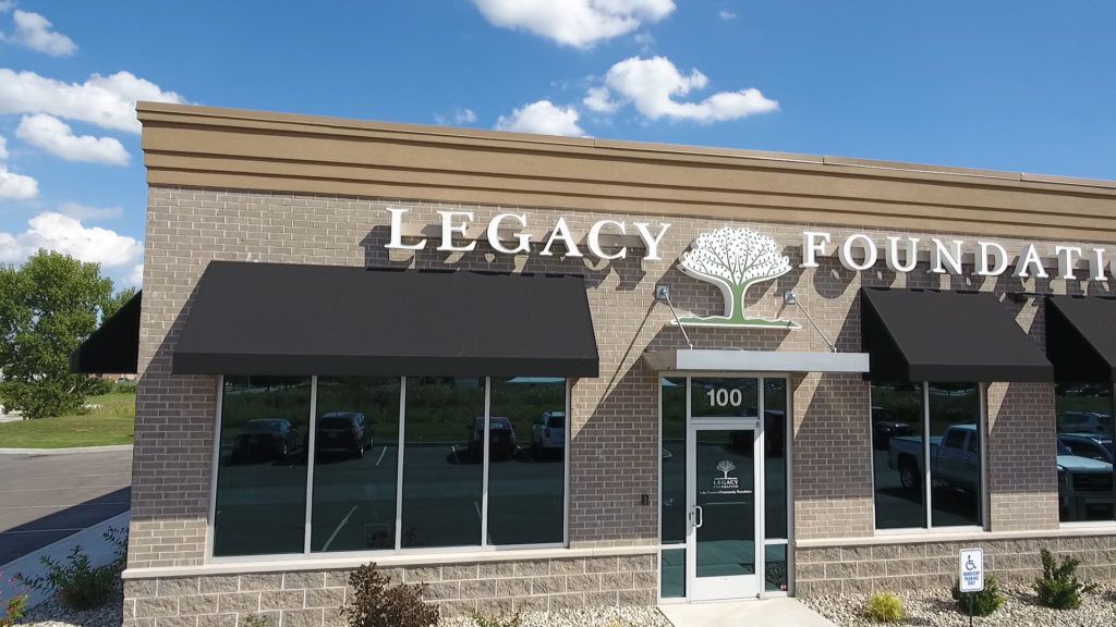 Legacy Foundation storefront with stone facade, black awning, and glass entrance under a blue sky