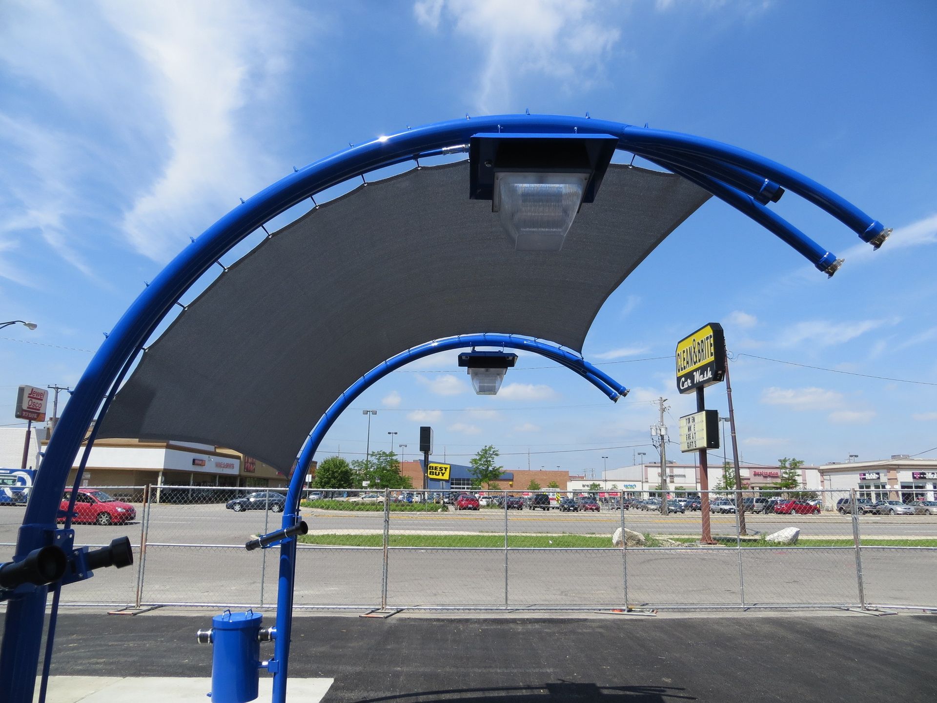 Blue curved bus stop shelter with benches beside a road under a bright sky