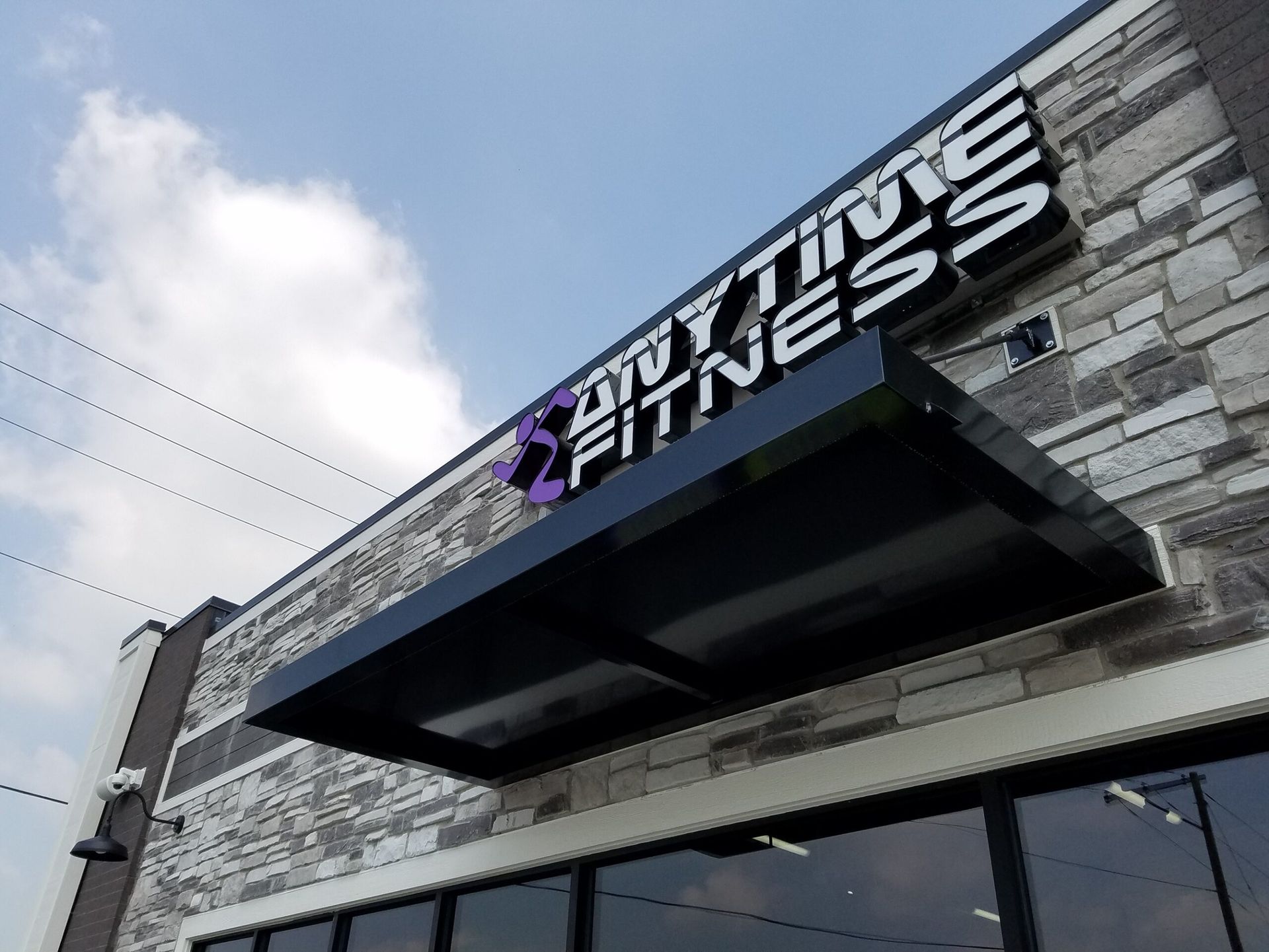 Building entrance for Anytime Fitness with black awning and stone facade, viewed from below