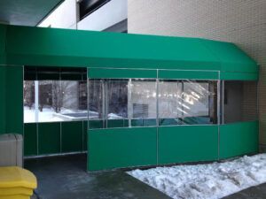Green glass entrance with sliding doors and snow piled outside under an overhang