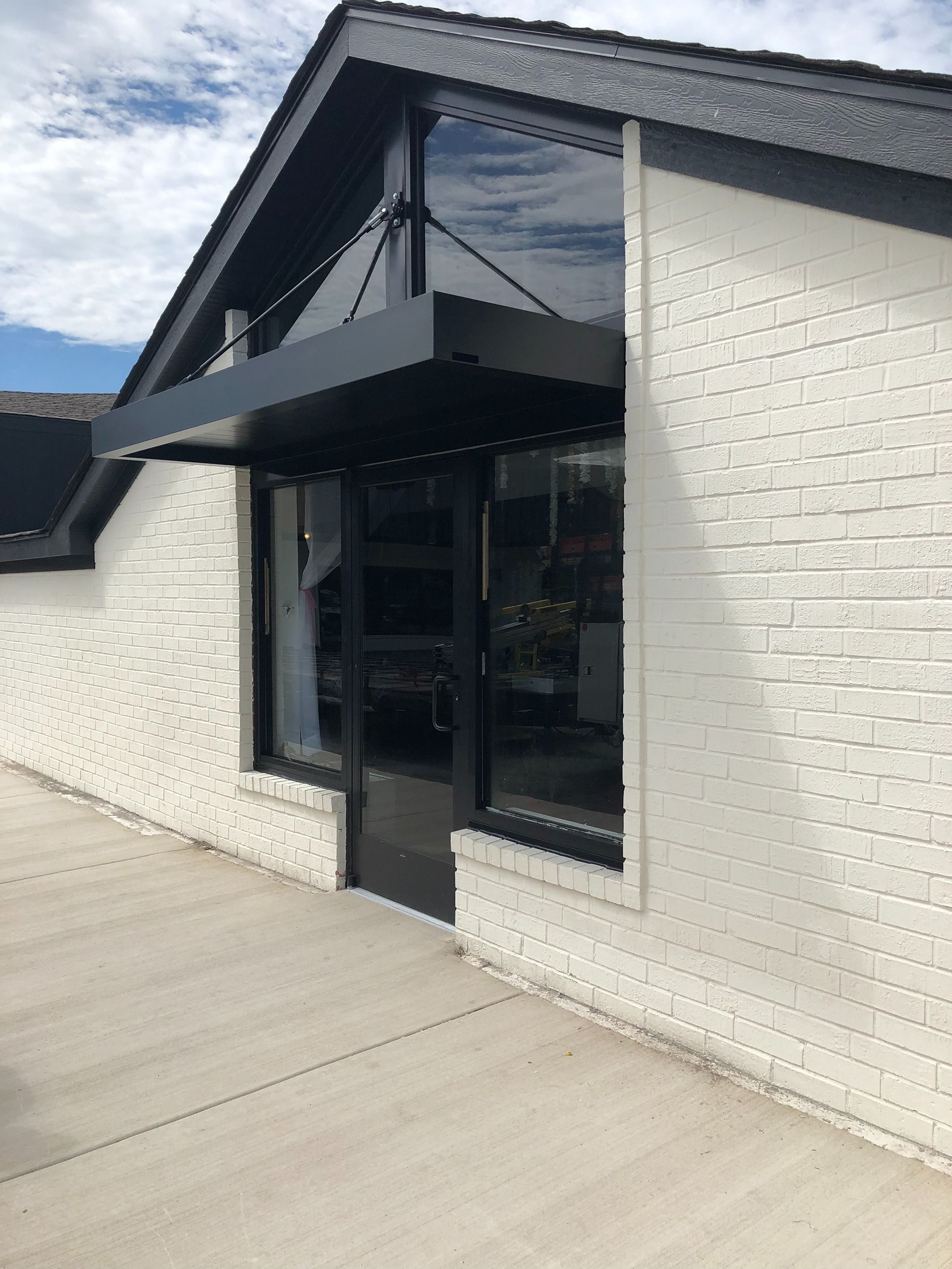 Modern white brick building with black awning and large glass windows along a concrete walkway