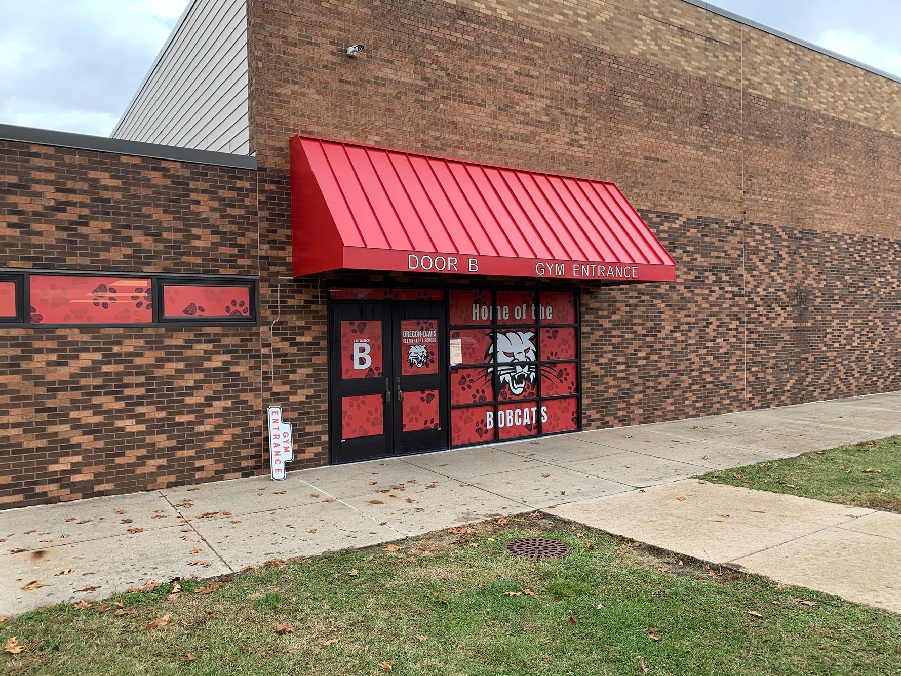 Brick storefront with red awning and glass doors, viewed from the sidewalk.