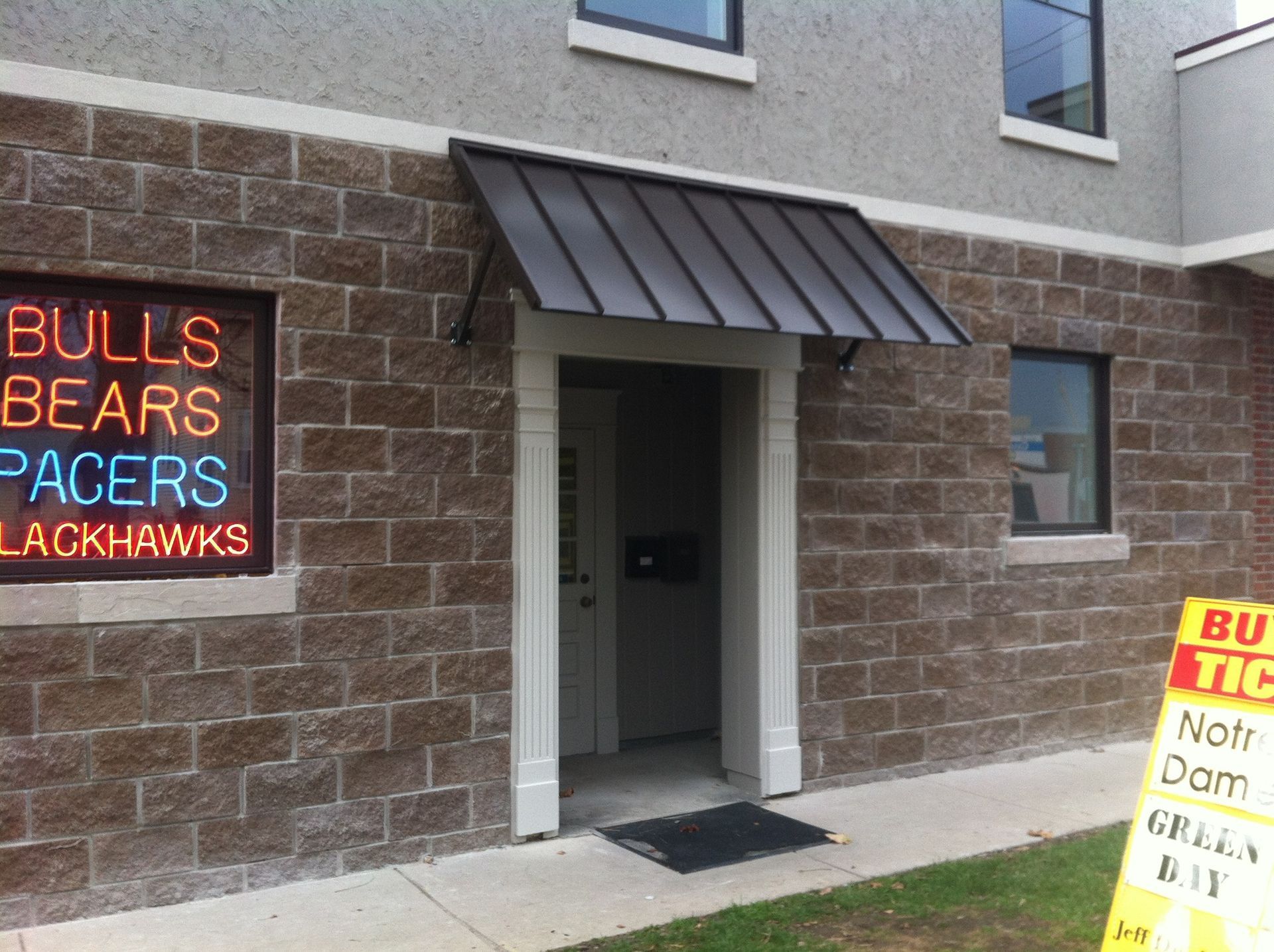 Exterior wall with illuminated team names and a doorway under a small awning