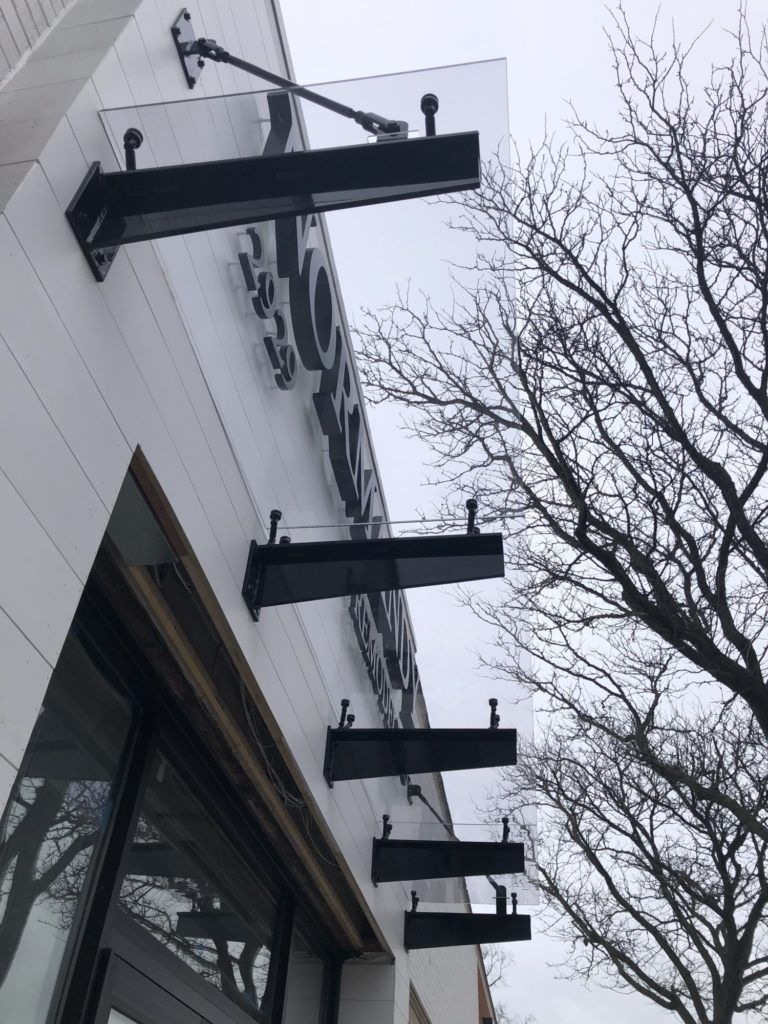 Black metal awnings on a white building beside leafless trees on an overcast day