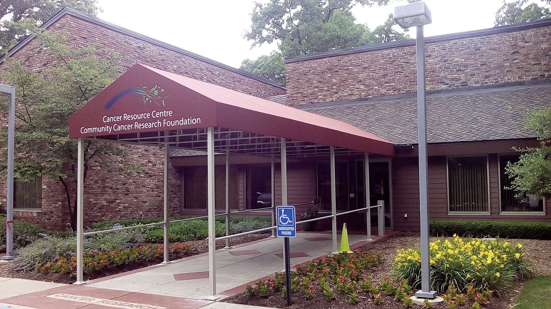Accessible building entrance with red canopy, wheelchair sign, and covered walkway surrounded by greenery