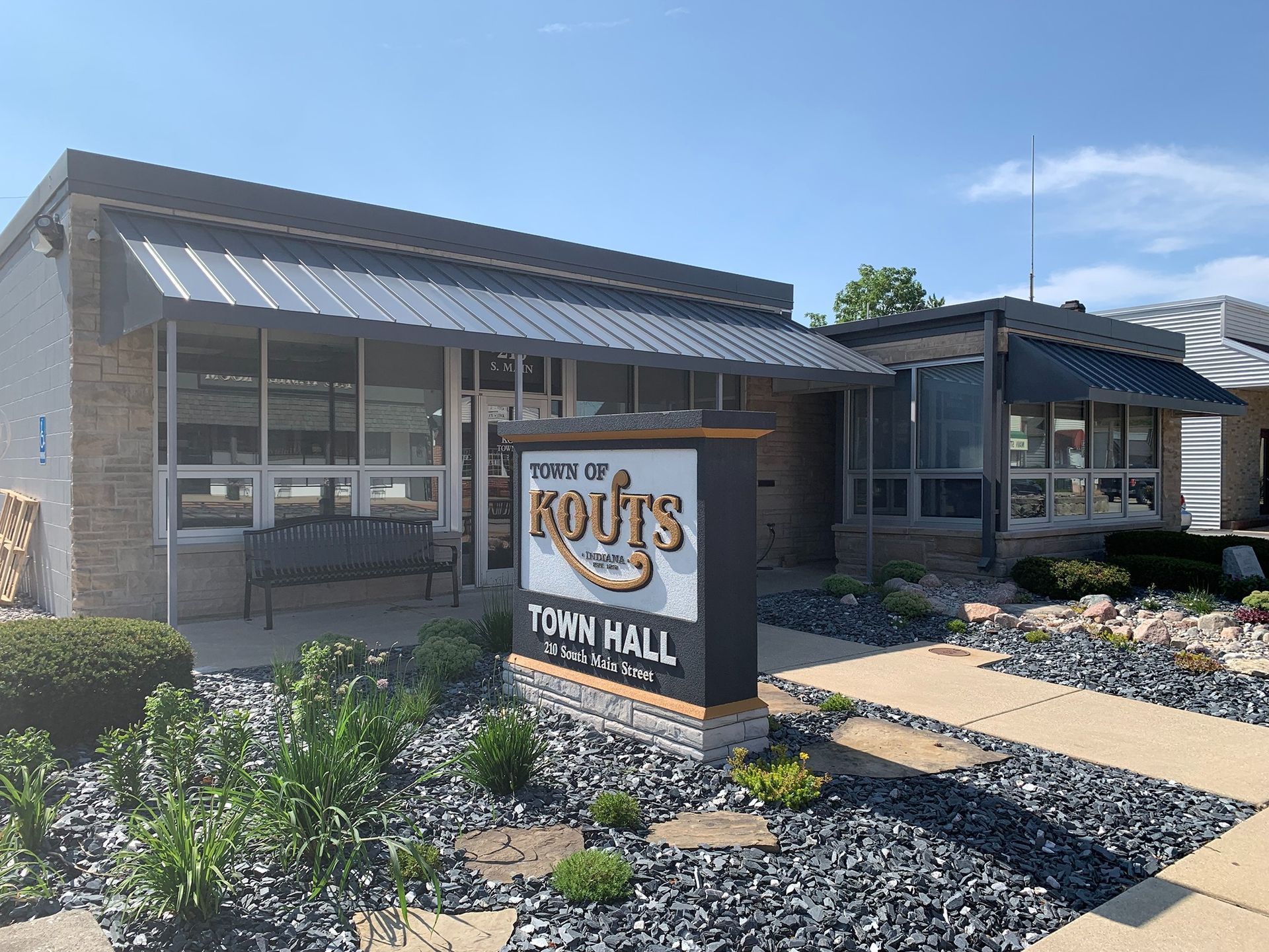 Town hall building with a sign reading “The Rots Town Hall” in front of a landscaped walkway.