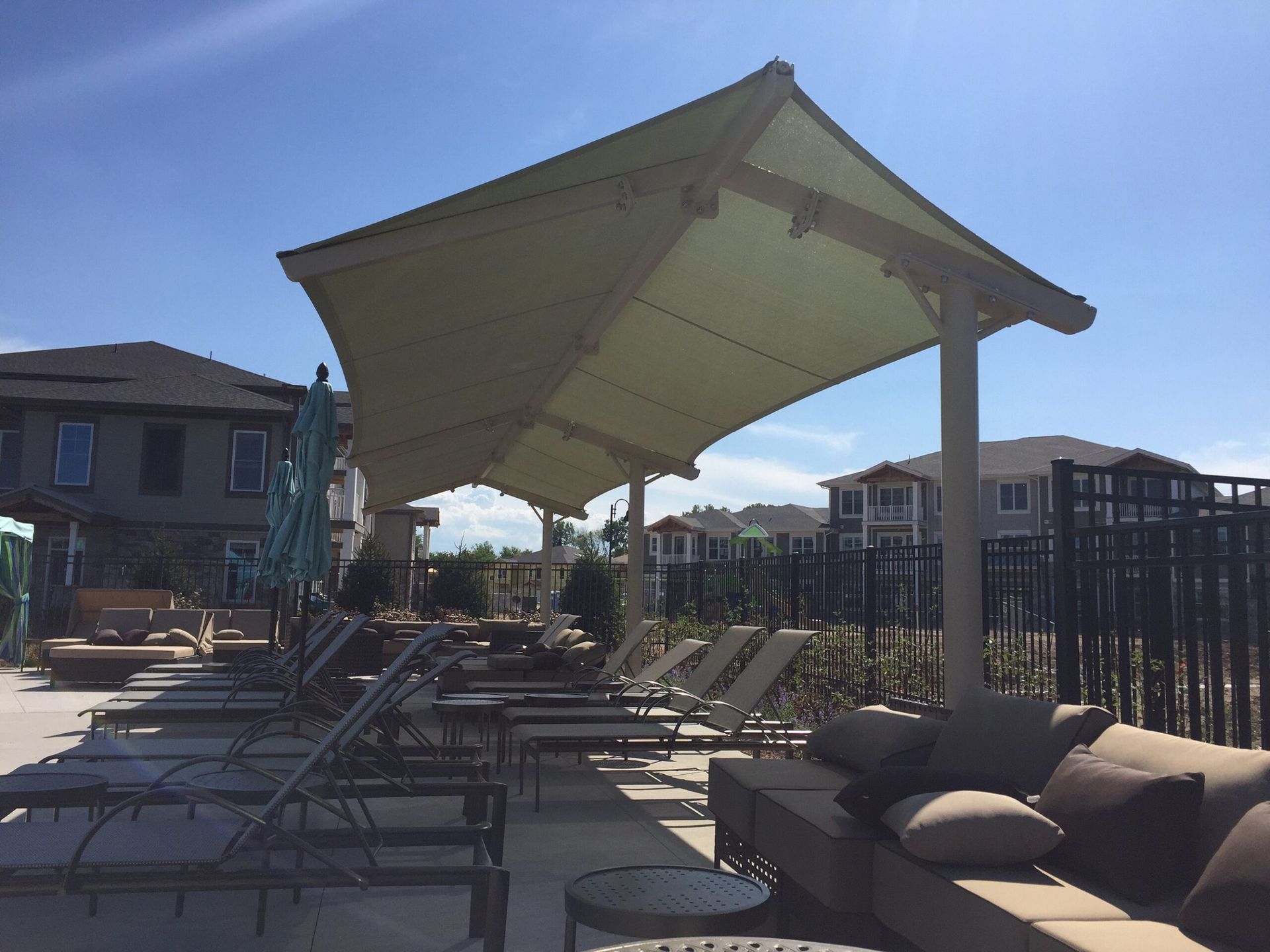 Outdoor poolside lounge with black chairs and a large canopy under a clear blue sky