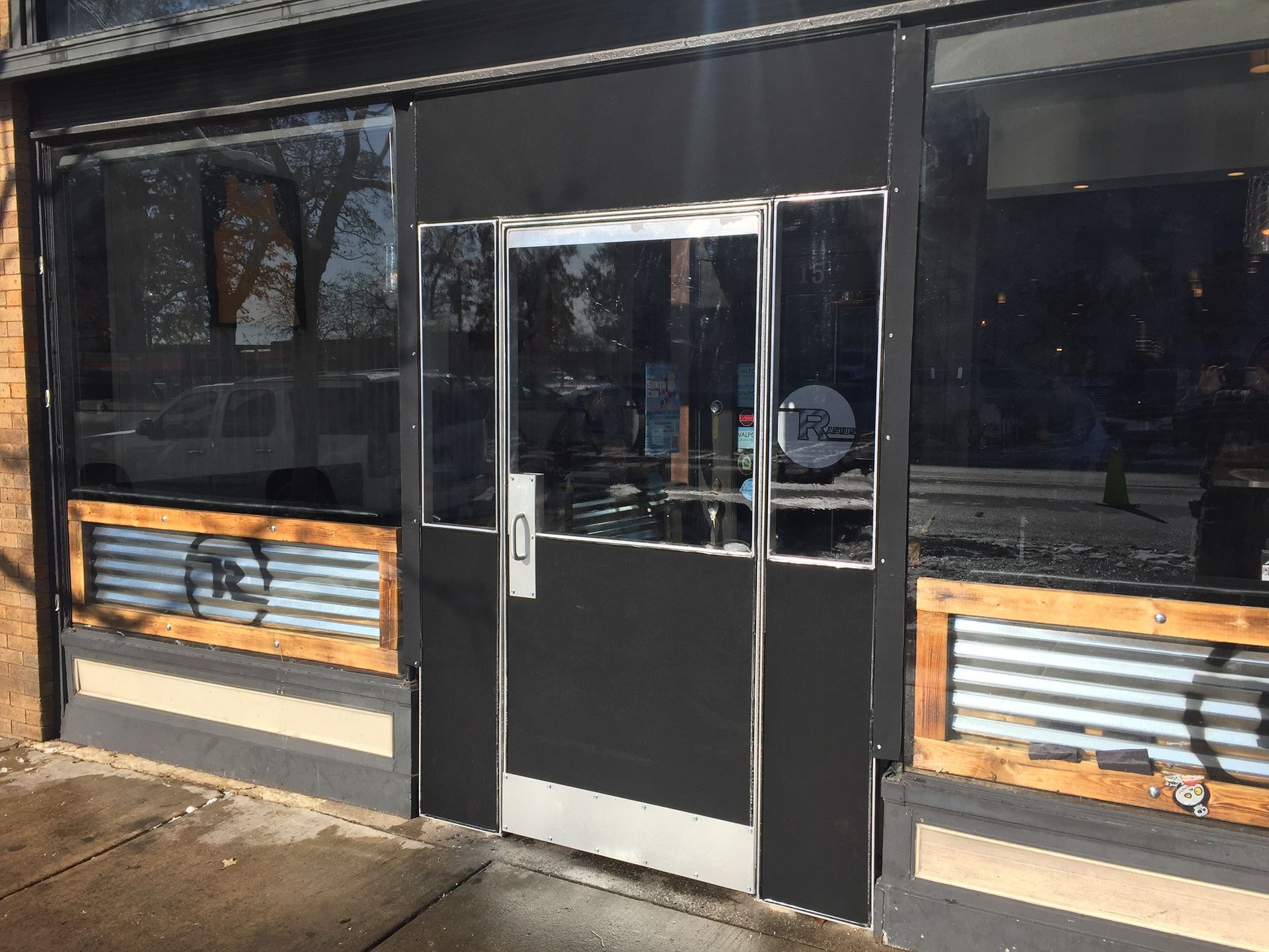Front entrance of a storefront with black doors and windows, framed by wood slat panels.