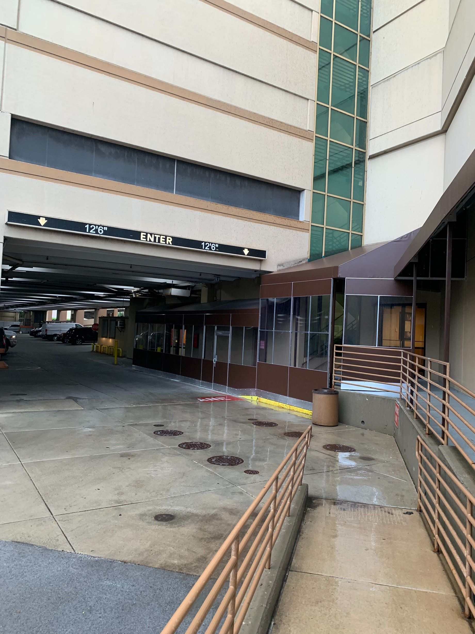 Covered parking lot entrance beside a building, with metal railings and wet pavement.
