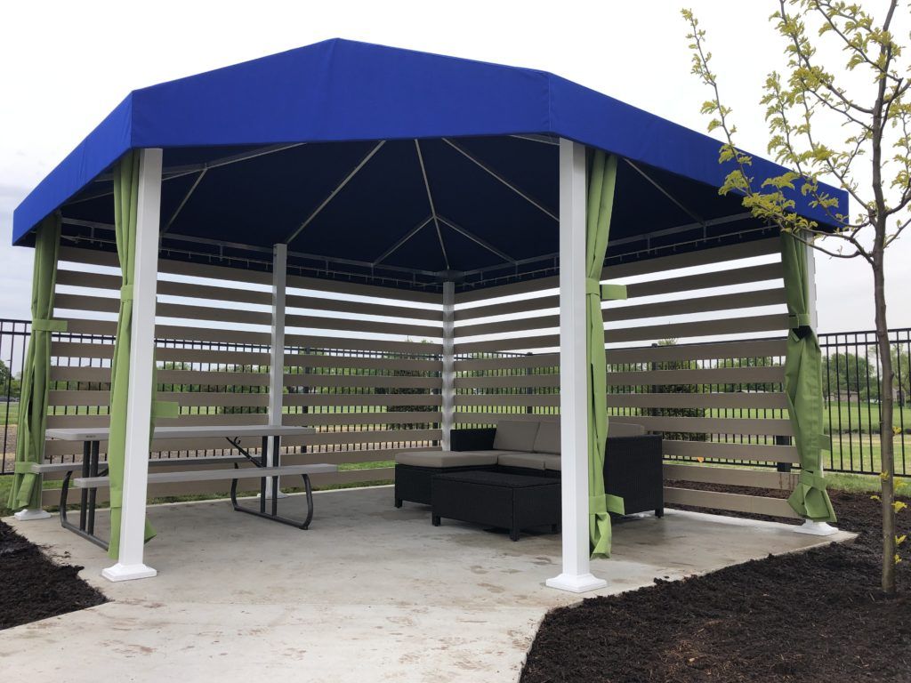 Open-sided blue-roofed gazebo with benches and picnic table in a landscaped outdoor area