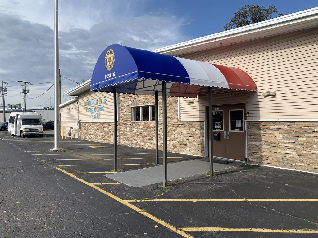 Blue-red awning over a building entrance with a wheelchair-accessible ramp and parking lines nearby