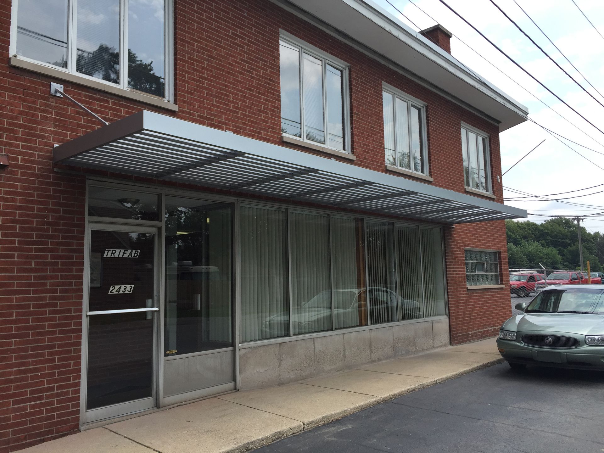 Brick storefront with striped awning, large windows, and a parked car on the right.