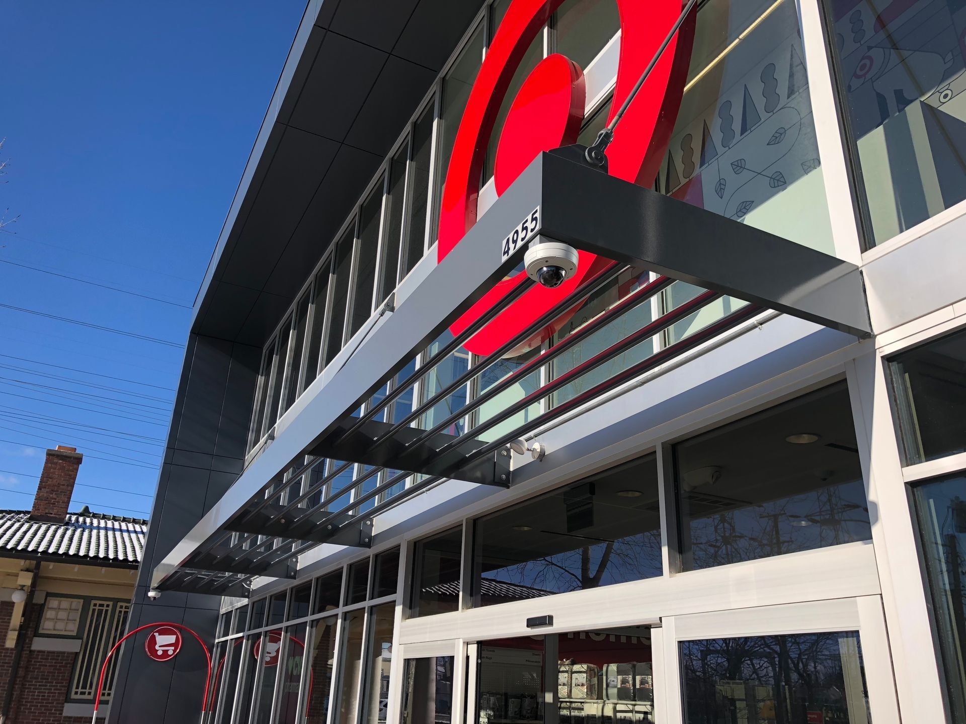 Modern building entrance with glass doors, metal awning, and large red sign above the facade